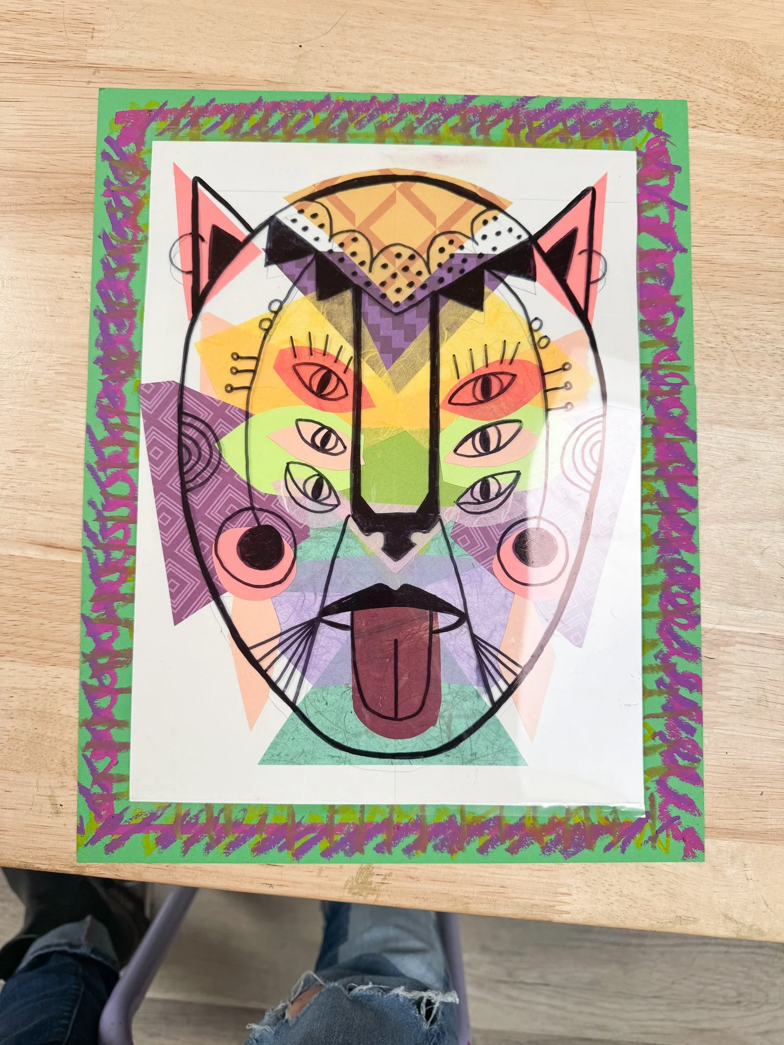 Colorful abstract drawing of a lion's face with multiple eyes, ears, and a tongue sticking out, layered with various geometric patterns and border designs.