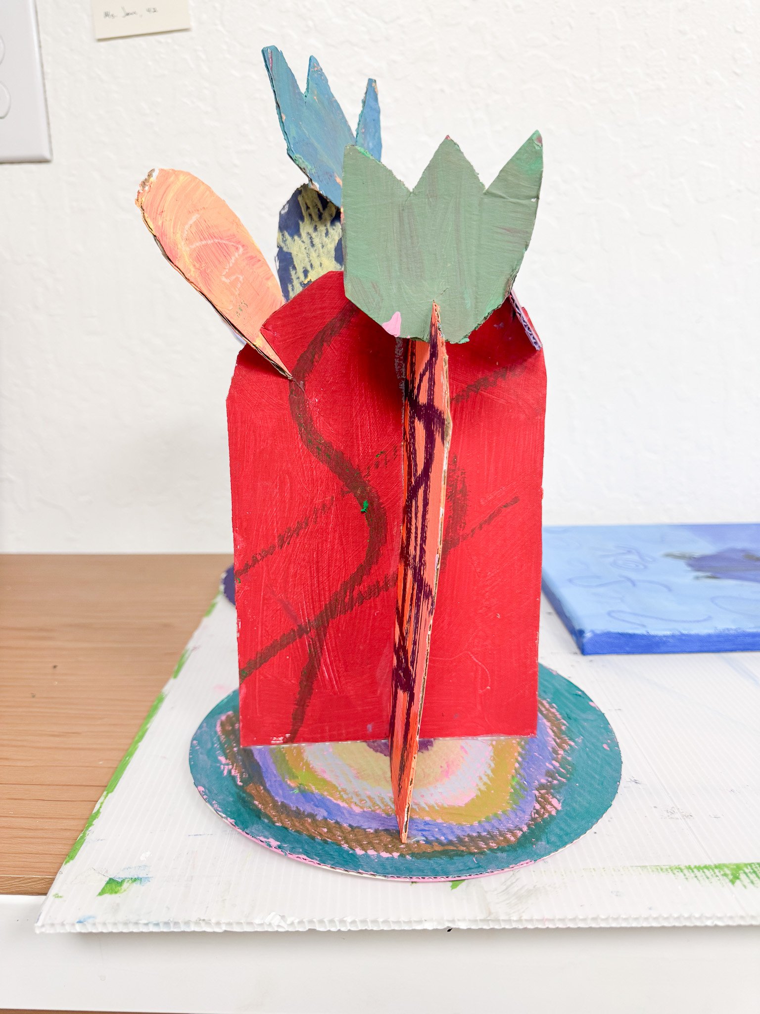 Colorful paper craft of a bouquet of tulips in a red vase on a white surface.