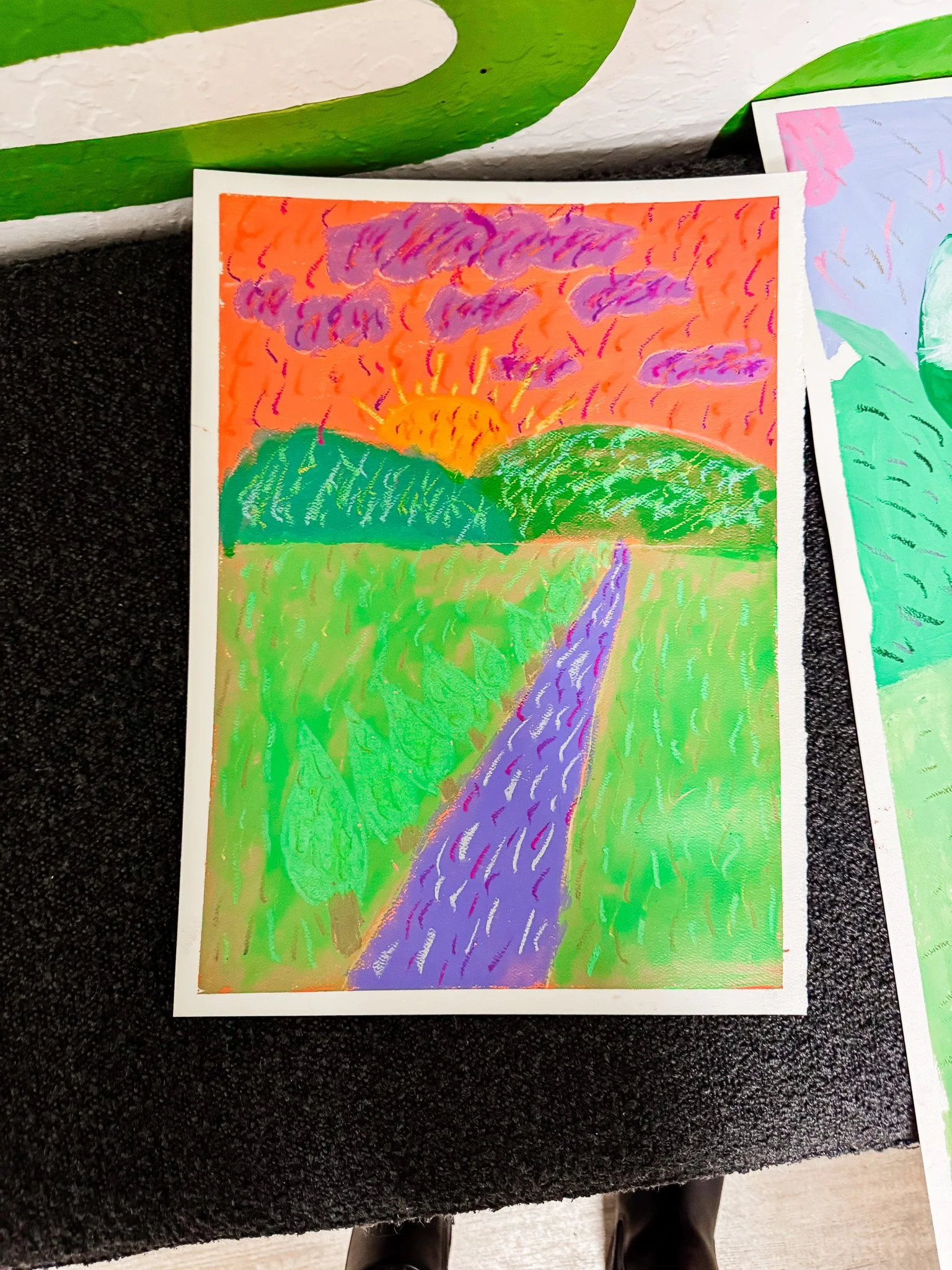 Colorful landscape drawing of a sunset over green hills, purple sky with clouds, purple river or road leading towards the horizon.