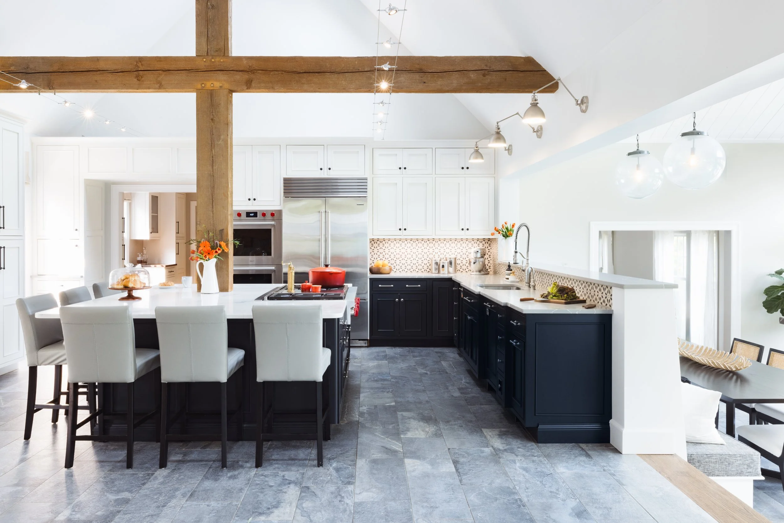 Modern kitchen with white and dark cabinets, large island, bar stools, wooden beam, stainless steel appliances, and decorative lighting.