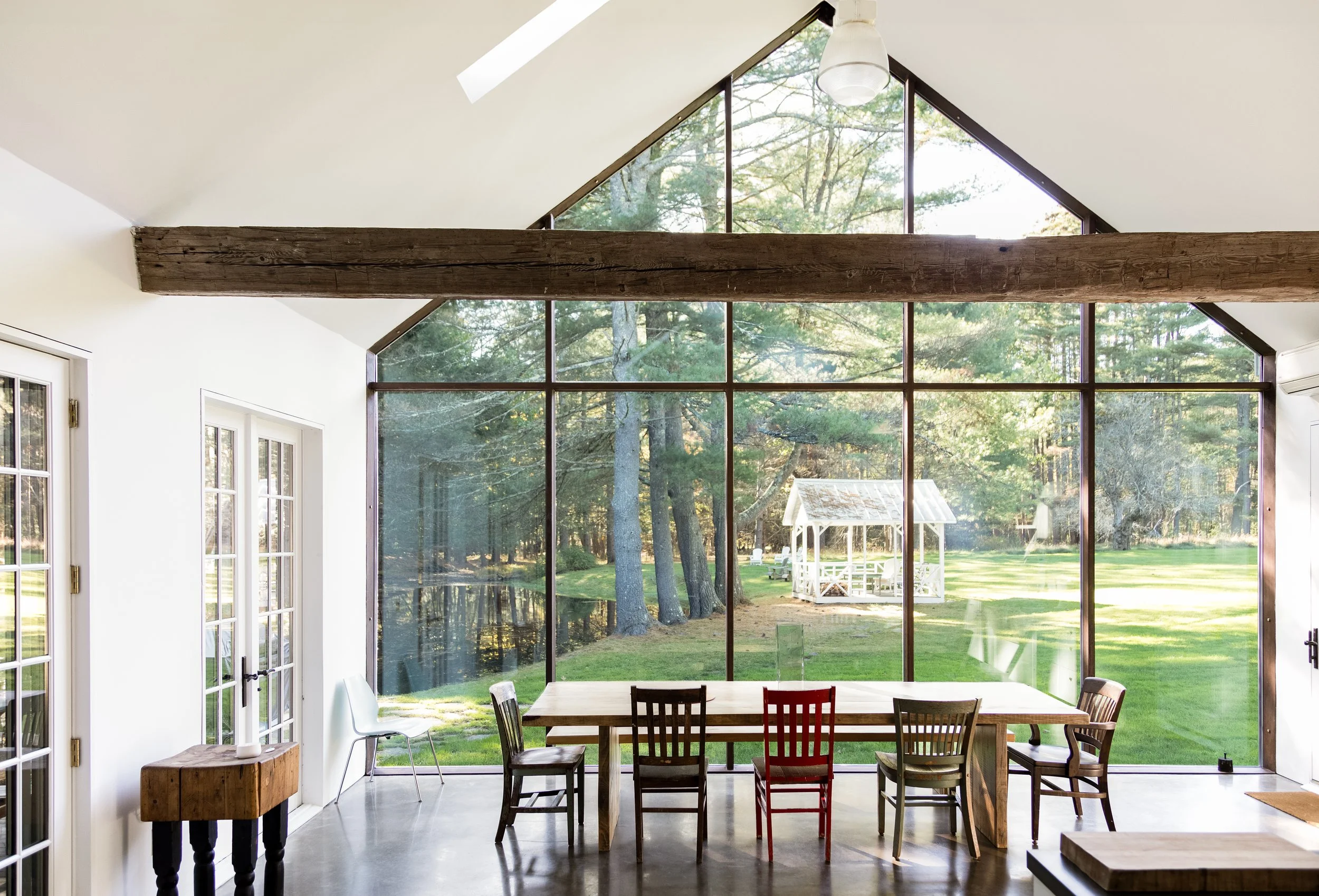 Modern dining area with large windows overlooking a green landscape with trees and a white gazebo.