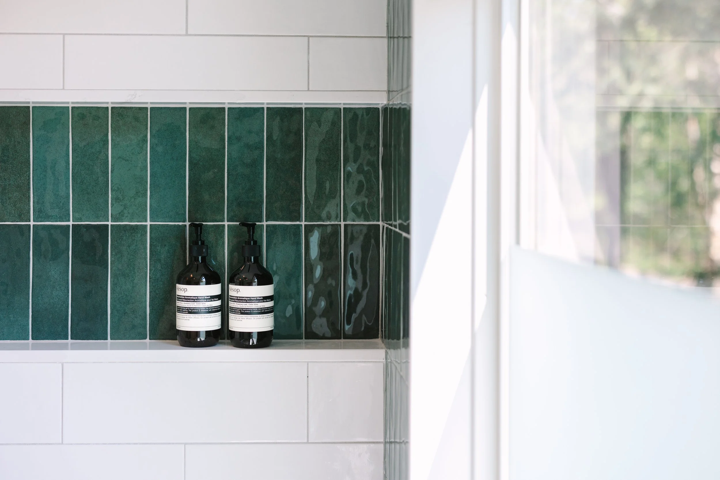 Modern bathroom shelf with green tiles and two bottles of liquid soap.