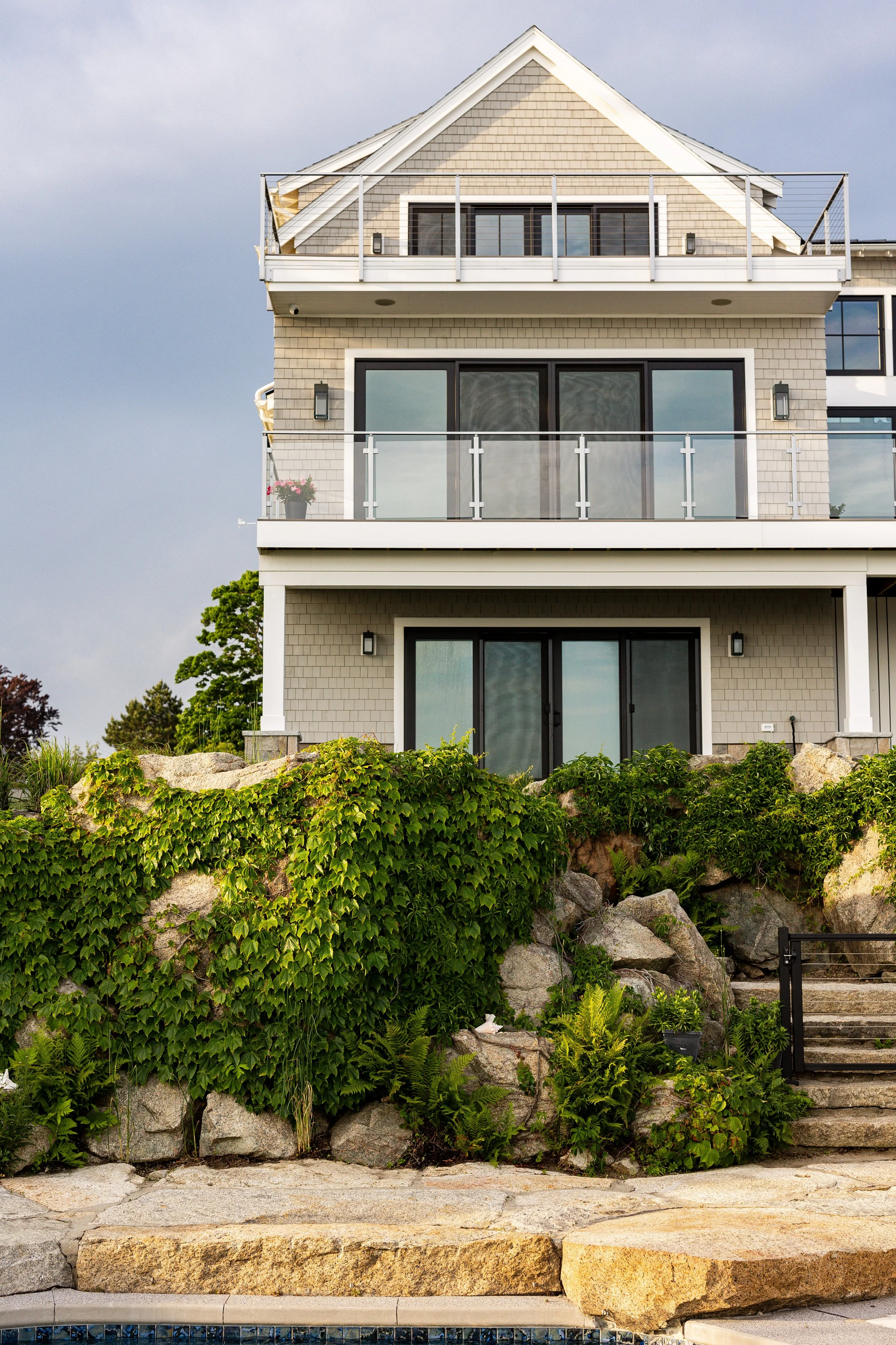Modern house with glass balconies, stone landscaping, and green ivy