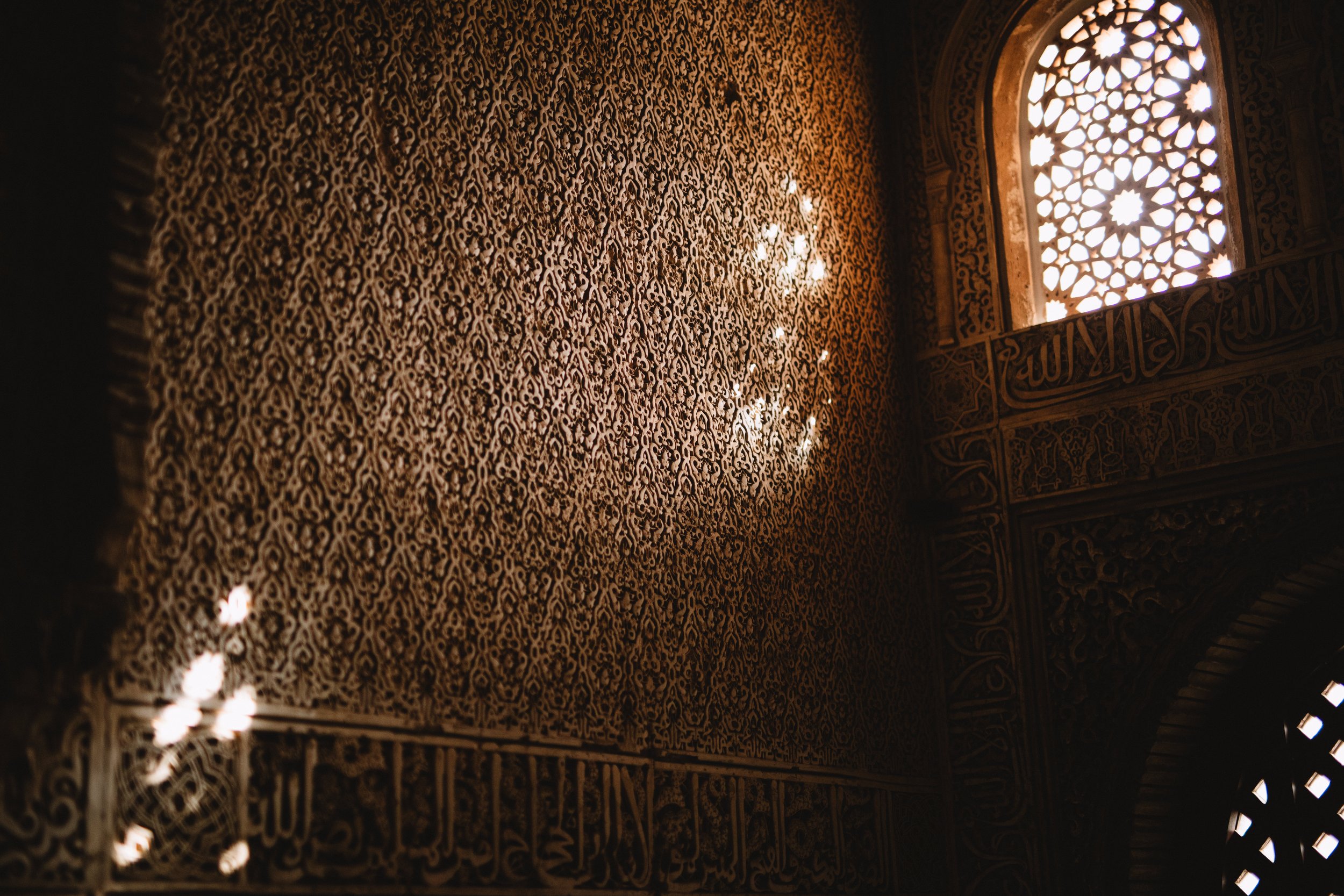 Intricate Islamic architectural pattern with sunlight filtering through a decorative window, casting light on the textured wall.