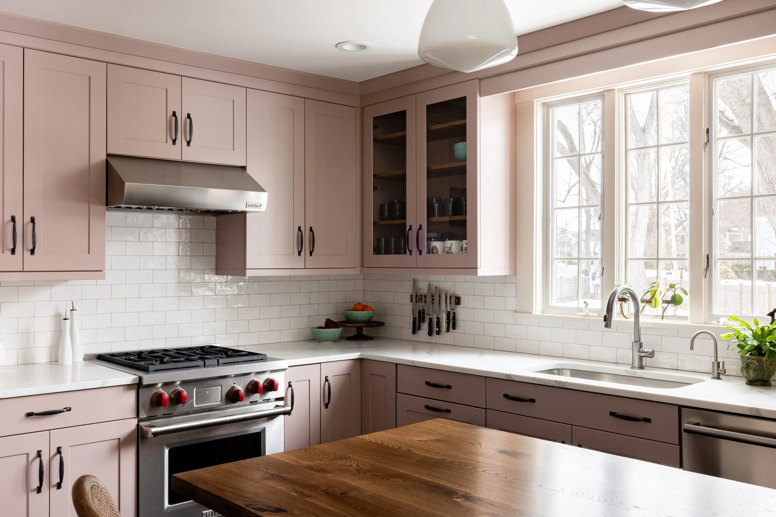 Modern kitchen with pink cabinets, stainless steel stove, and white tile backsplash.