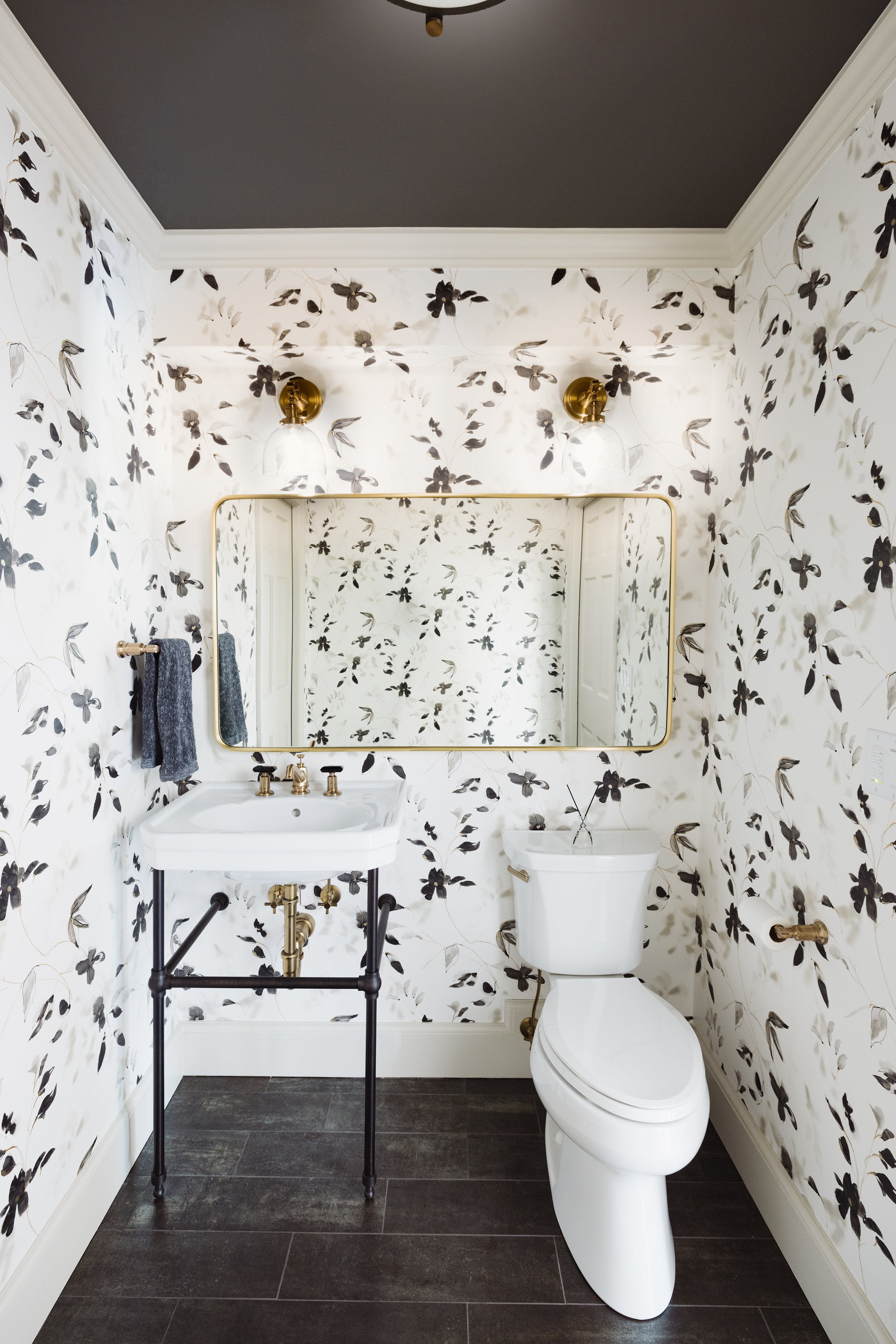 Small bathroom with floral wallpaper, white sink, mirror, toilet, and gold fixtures.