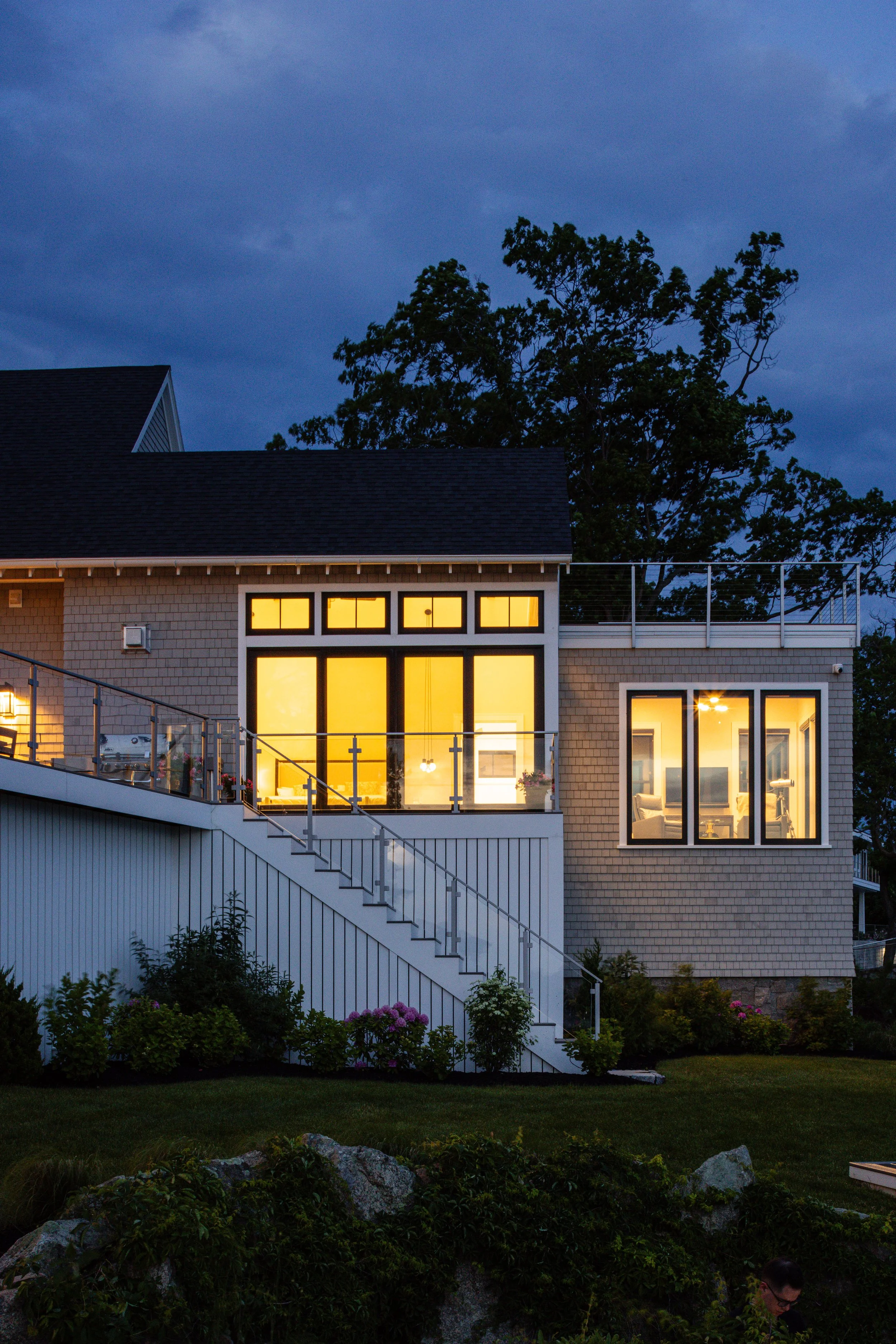 Modern house exterior at dusk with large illuminated windows and a staircase leading to a garden.