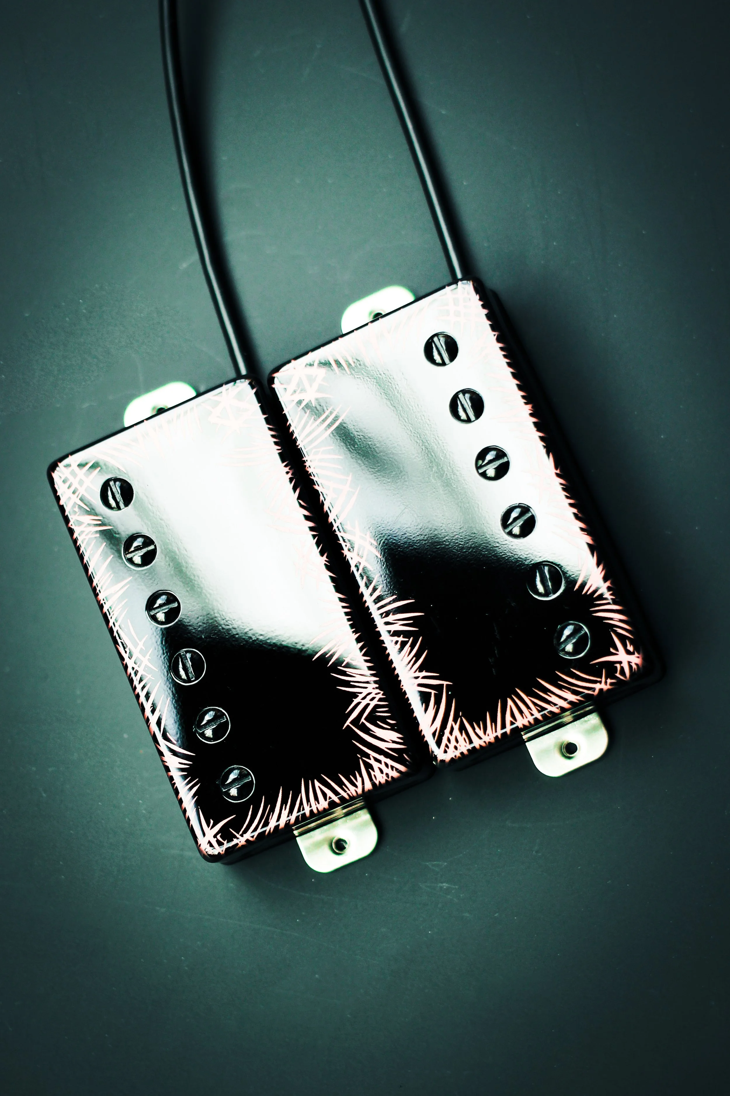 A pair of metallic electric guitar pickups with black screws and wires, placed on a dark surface.