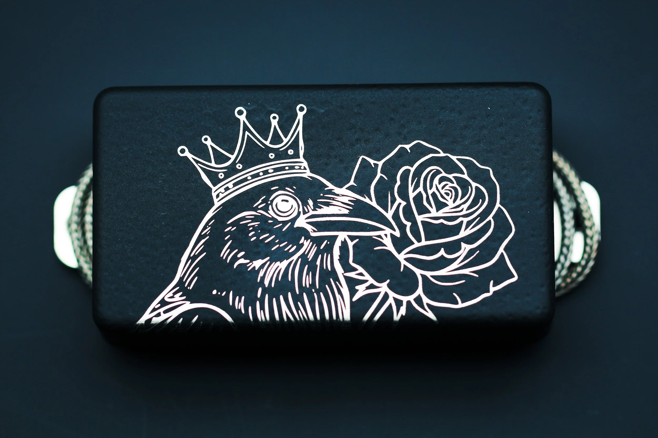 Satin black solid humbucker pickup cover with crow or raven with a crown and rose design.