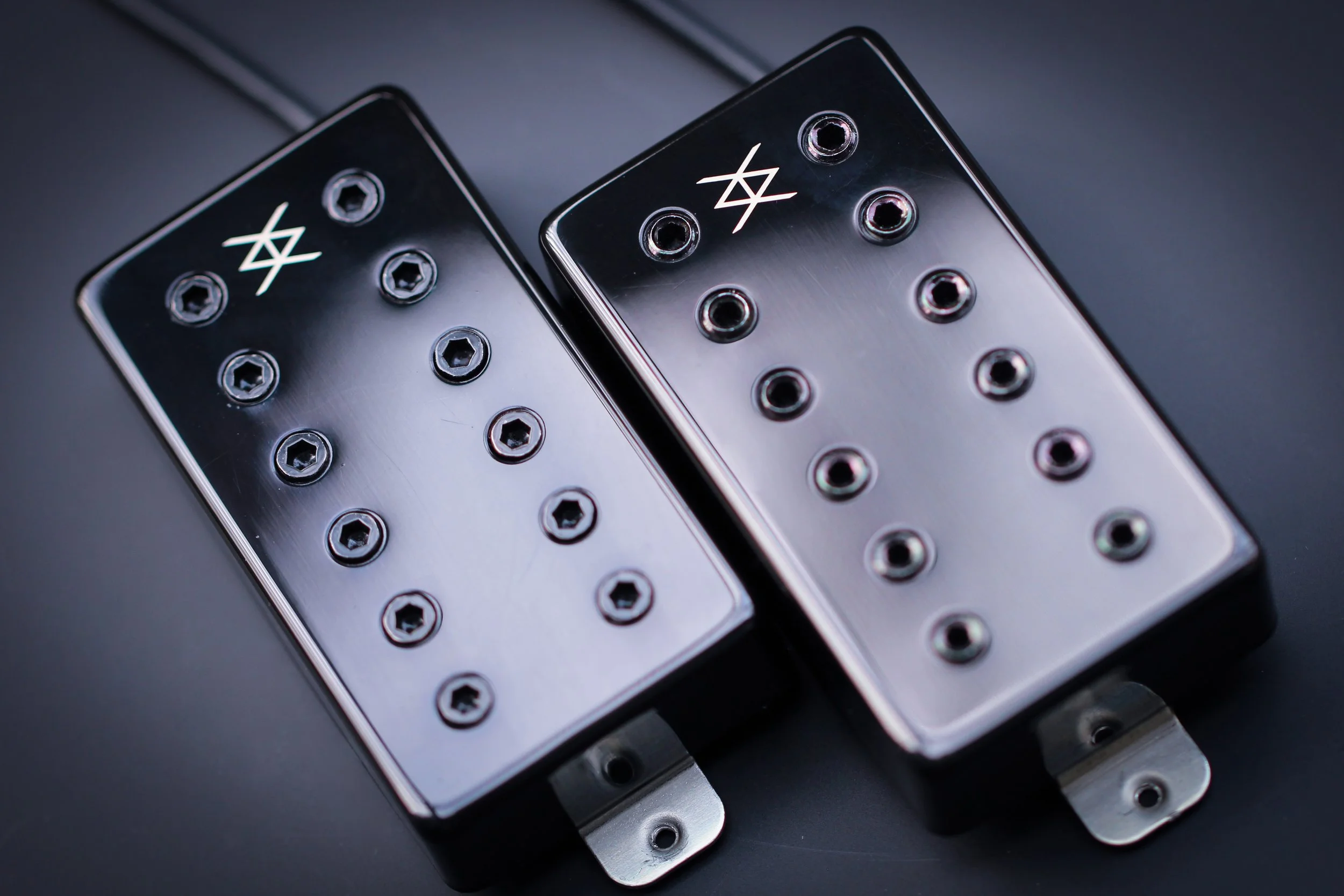Close-up of two guitar pickups with metal screws on a dark surface.