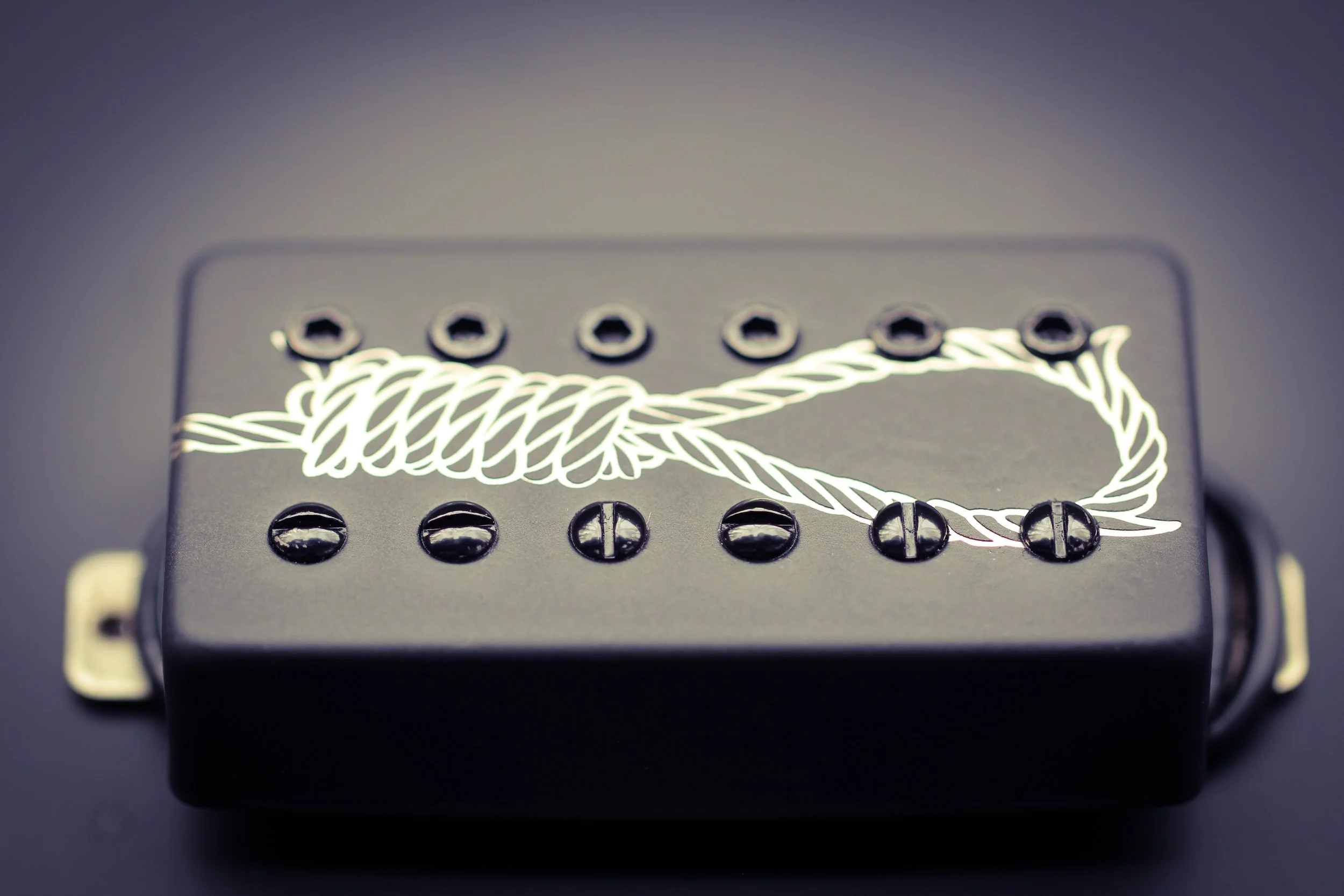 A black guitar pickup cover with a graphic of a noose made from a rope with a loop and knots.