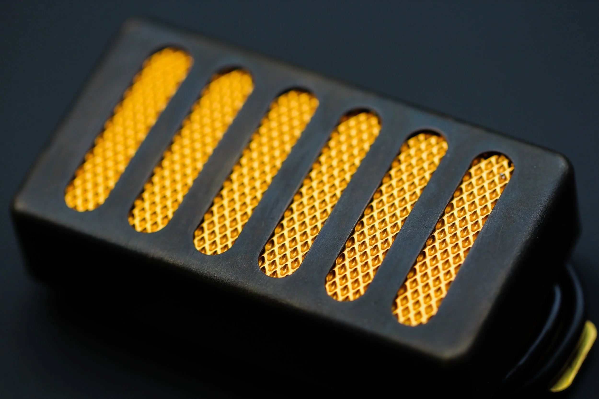 Close-up of a black rectangular object with a yellow, textured, grated surface visible through elongated oval cutouts.