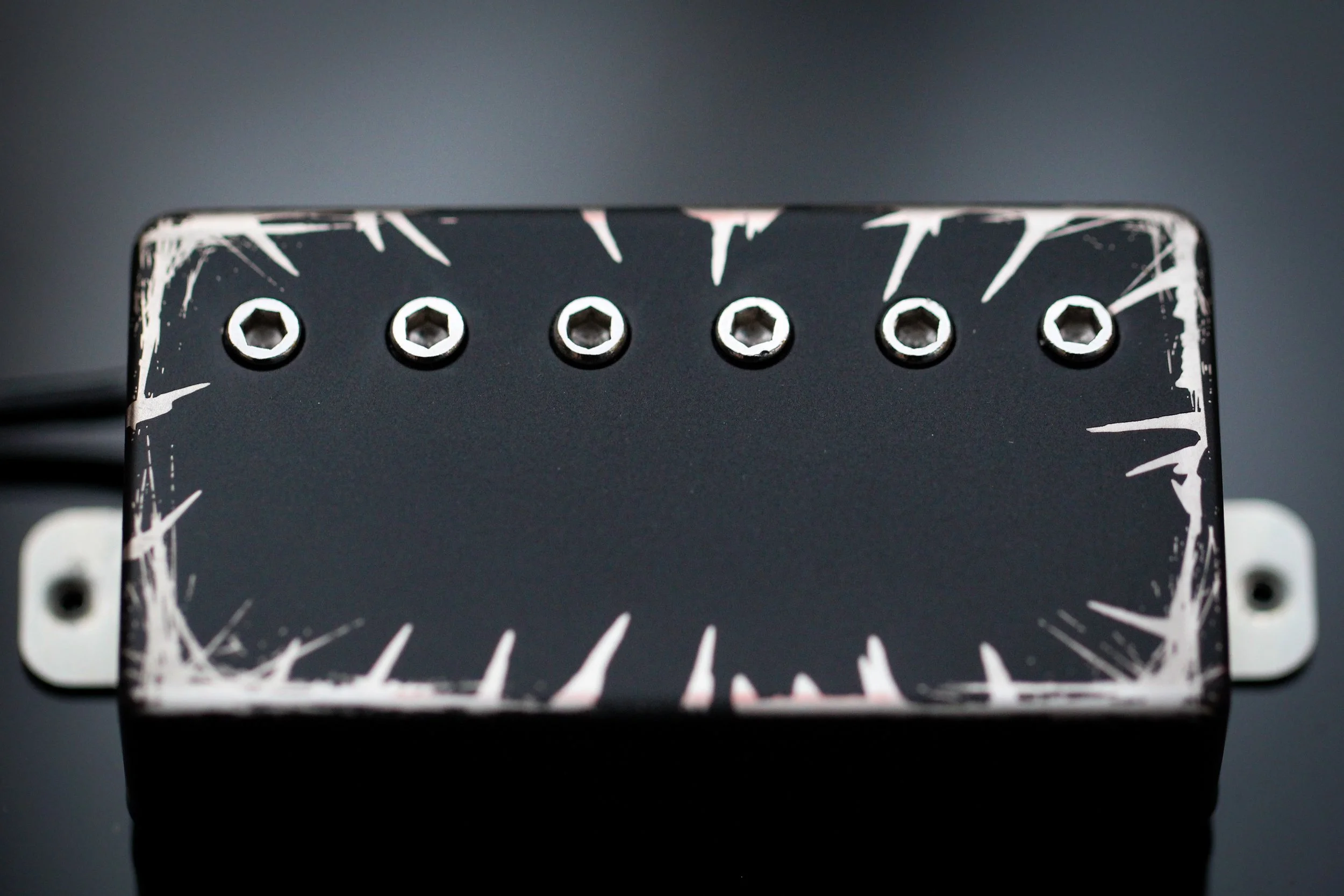 Close-up of a guitar effects pedal with six black knobs and a black surface, decorated with white streaks around the edges.