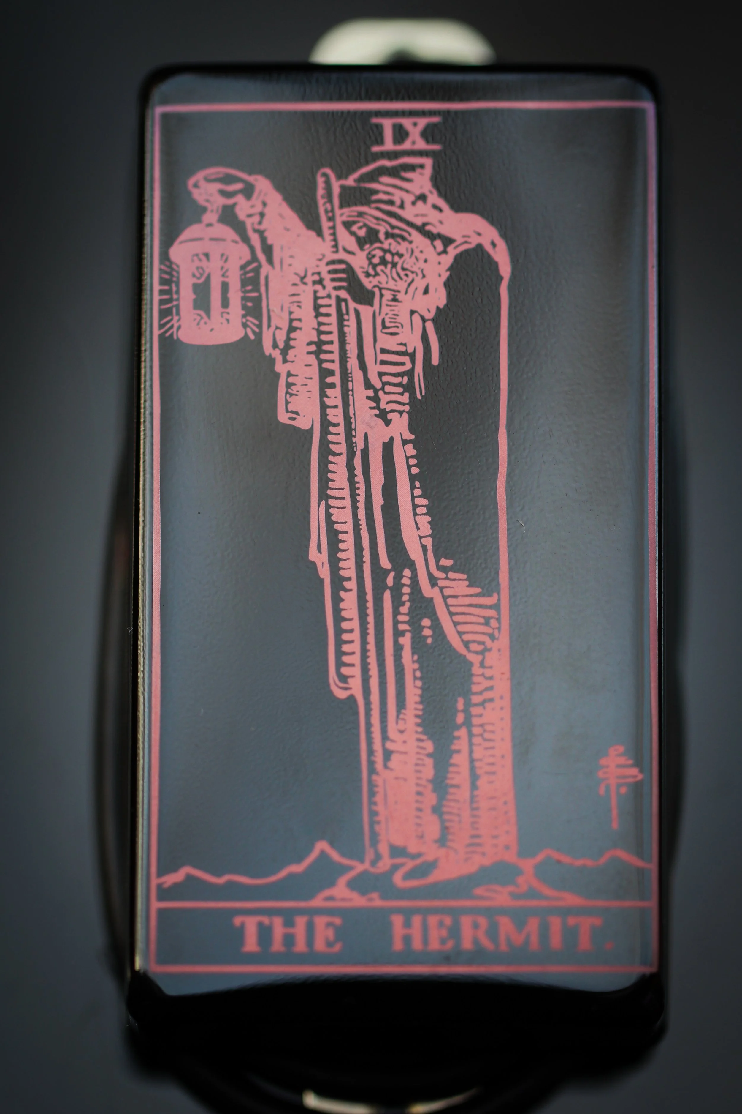 Solid black shiny humbucker pickup cover with an etch of the Tarot card The Hermit.