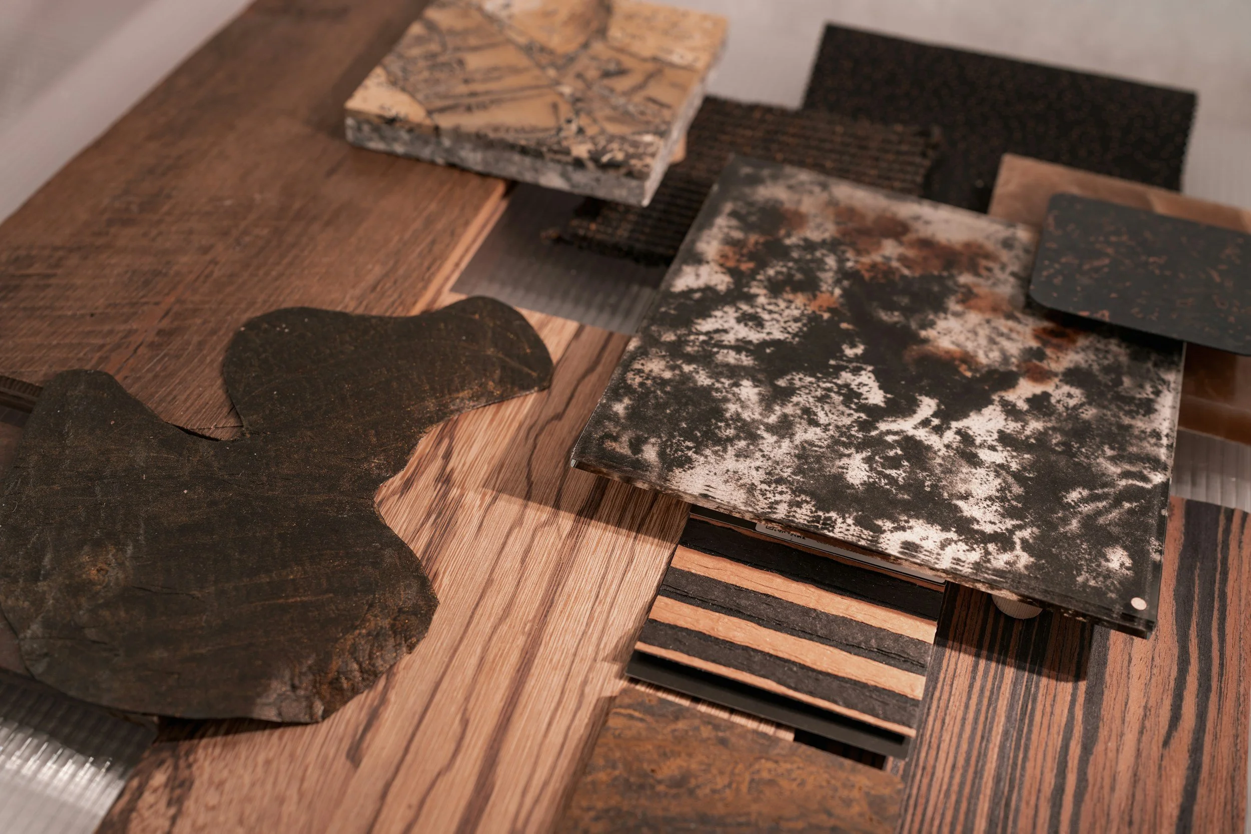 Samples of natural materials, including stone, dark slate, timber and metal, laid out on a wooden surface