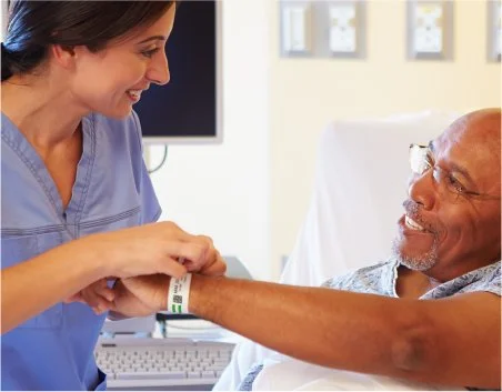 A nurse adjusts a patient's wristband in a hospital bed.