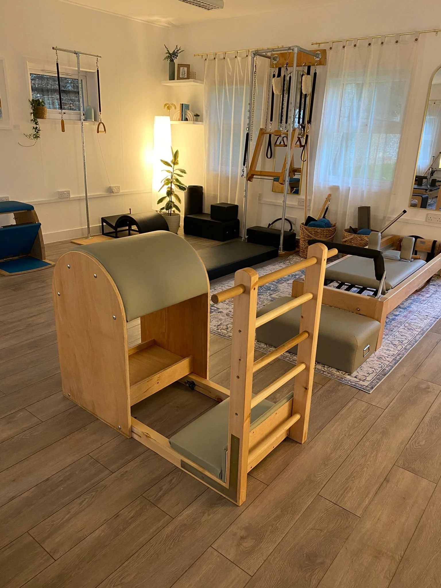 The Pilates Apparatus Studio at The Pilates Studios at Lavant House, featuring a Ladder Barrel, Wunda Chair, Reformers, and Tower against a softly lit backdrop of curtains and plants.