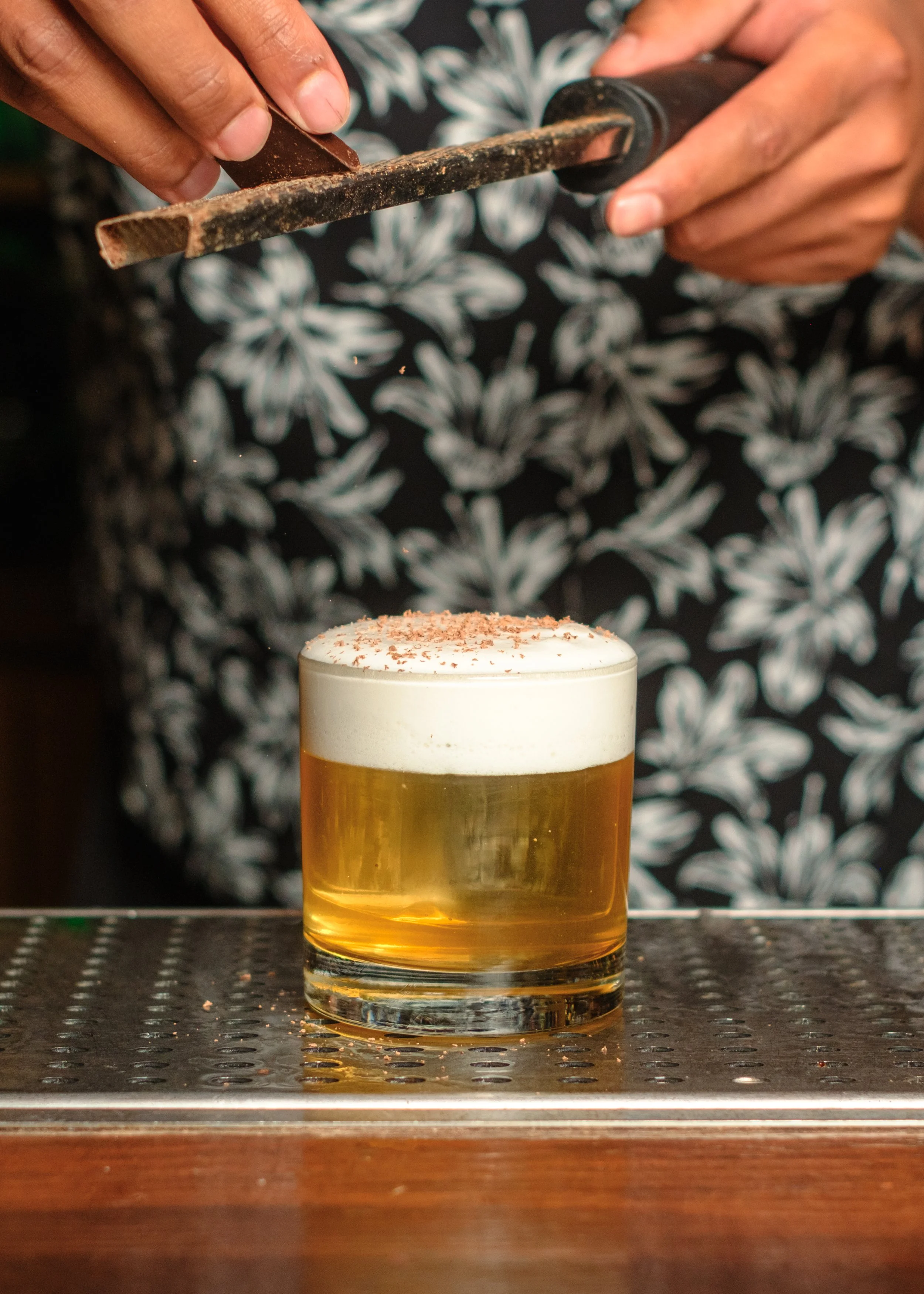 A person serving whipped cream with chocolate shavings onto a glass of beer.