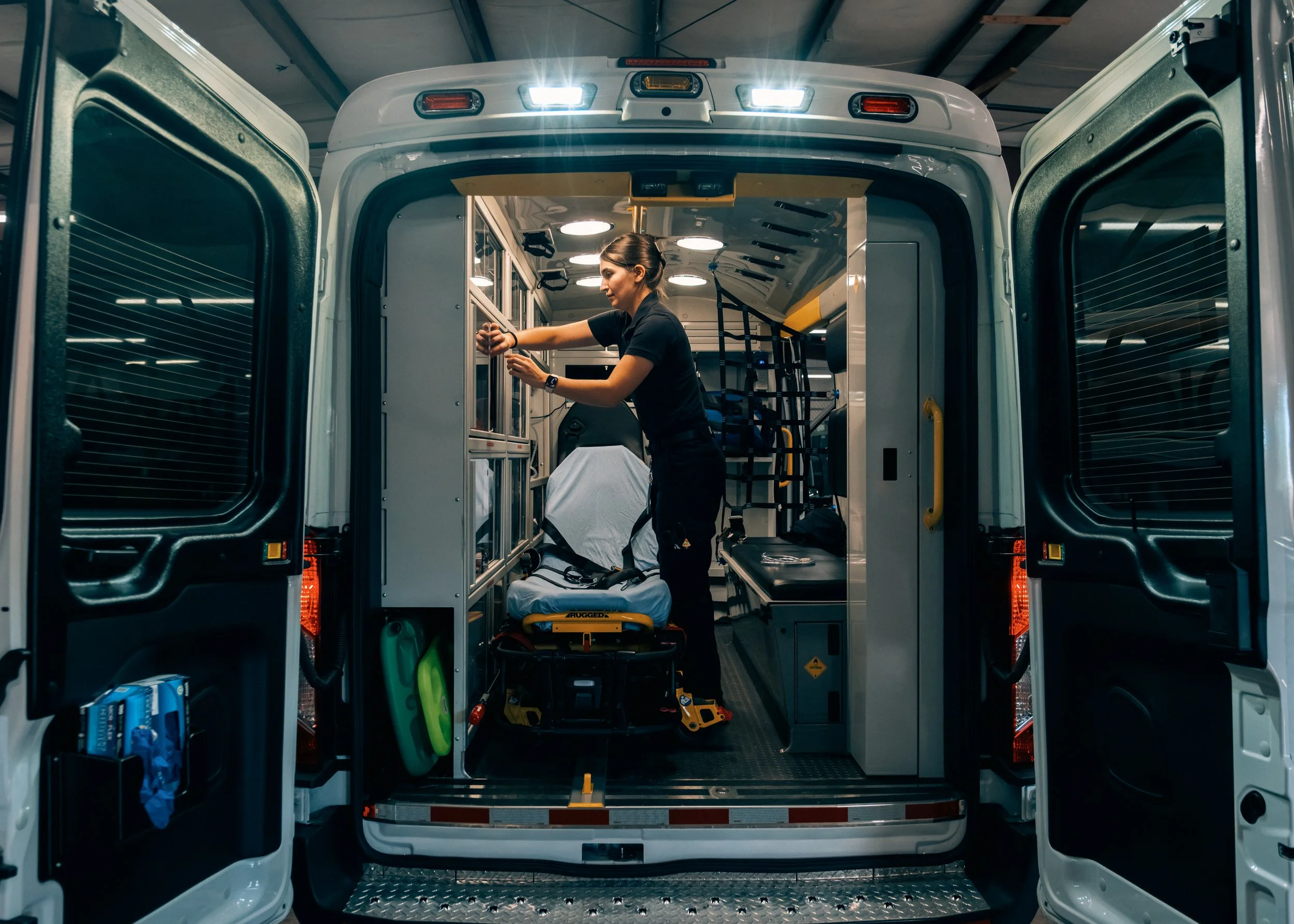 A paramedic woman working inside an ambulance, attending to medical equipment near a stretcher.