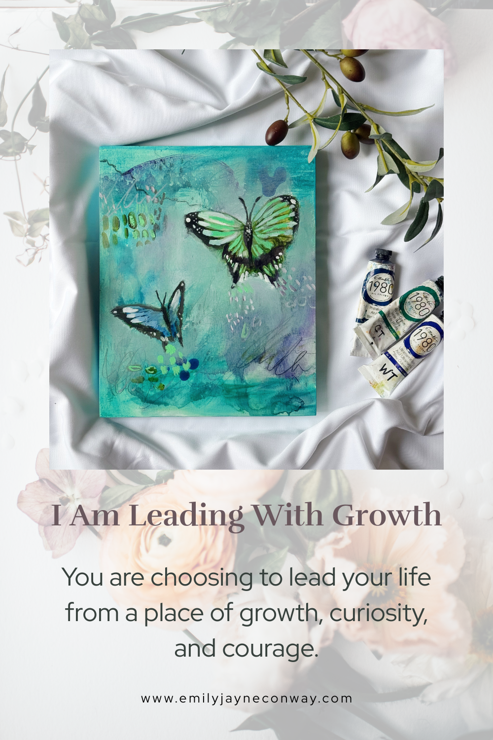 A painting of two butterflies, one green with black accents and one blue with black accents, on a teal background with abstract elements, surrounded by art supplies including tubes of paint, on a satin cloth with leafy branches and olives overhead.