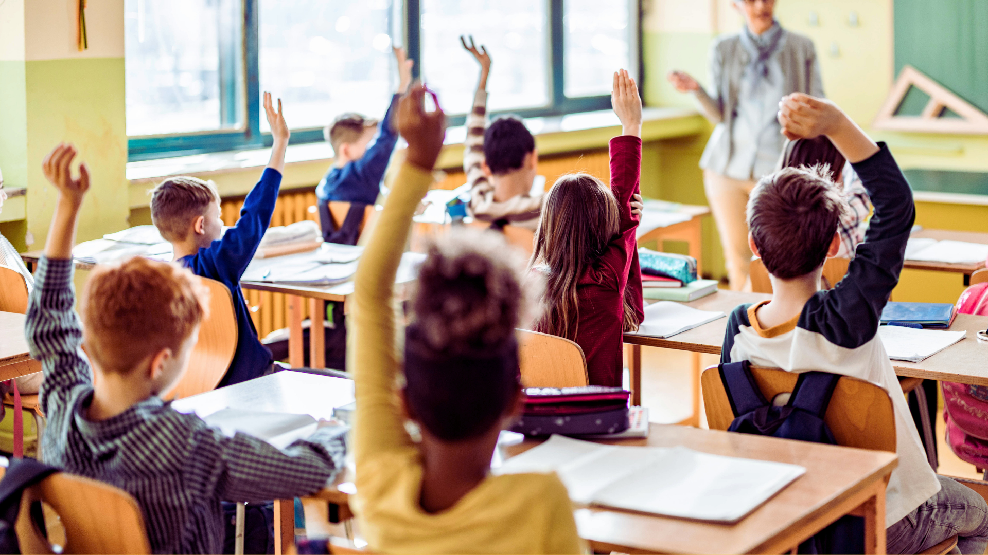 Classroom with students at desks raising hands