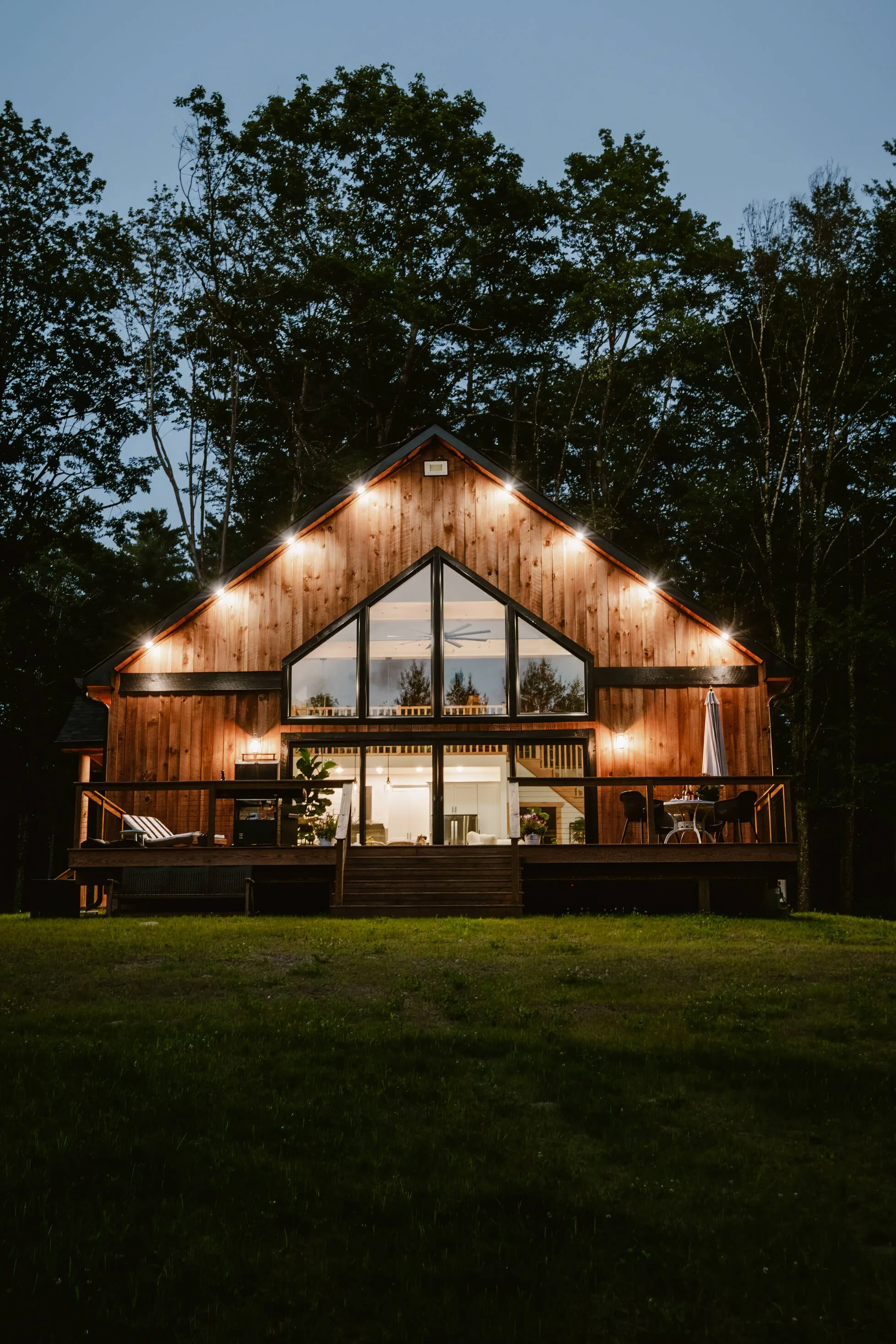 Stunning dusk exterior of a Catskills A-frame Airbnb cabin with glowing lights, surrounded by trees.