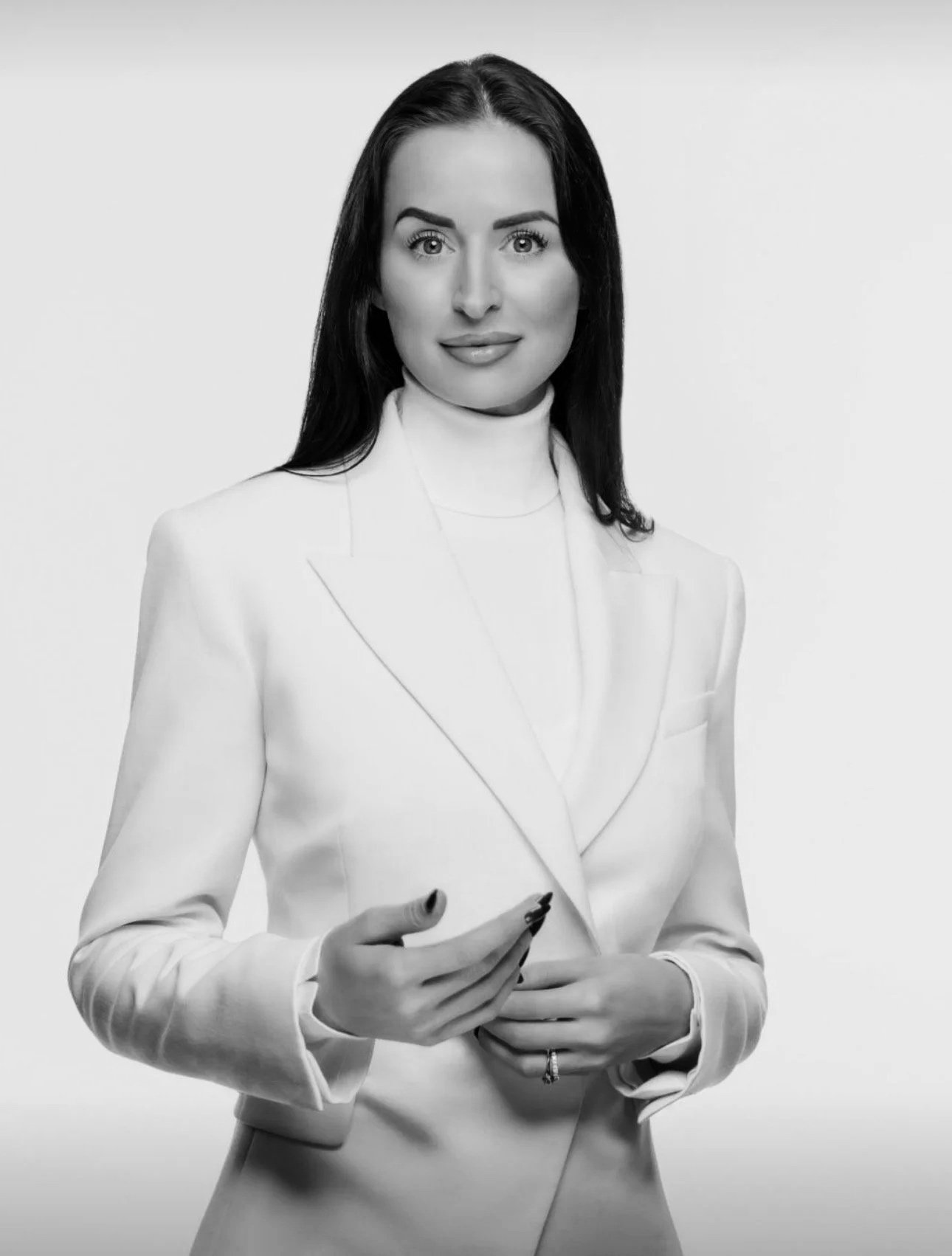 Schwarz-Weiß-Fotografie einer professionellen Frau in einem weißen Blazer, die ein Smartphone hält.