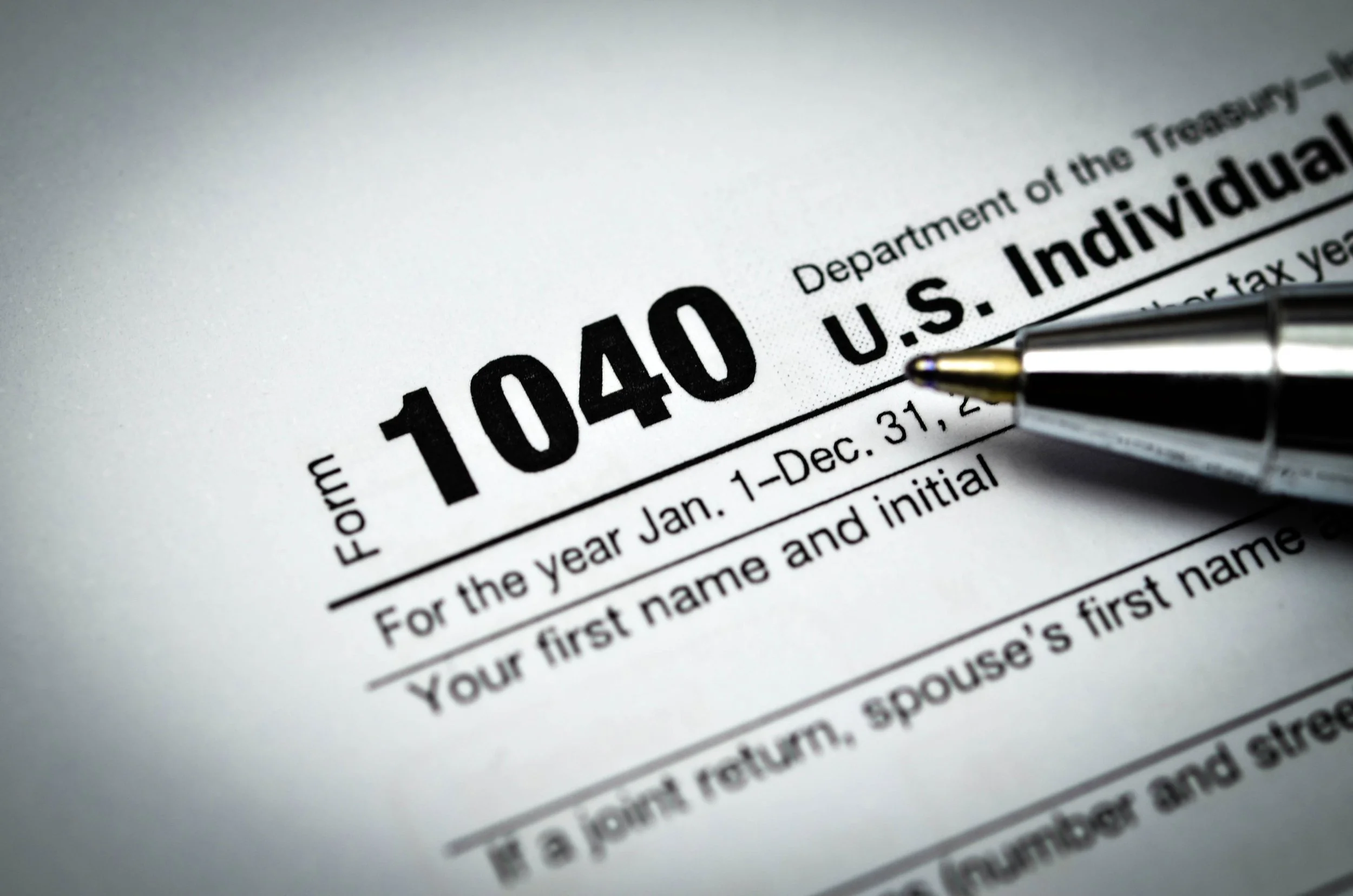 Close-up of a tax form labeled 1040 U.S. Individual, with a pen pointing to the section for the taxpayer's first name and initial.