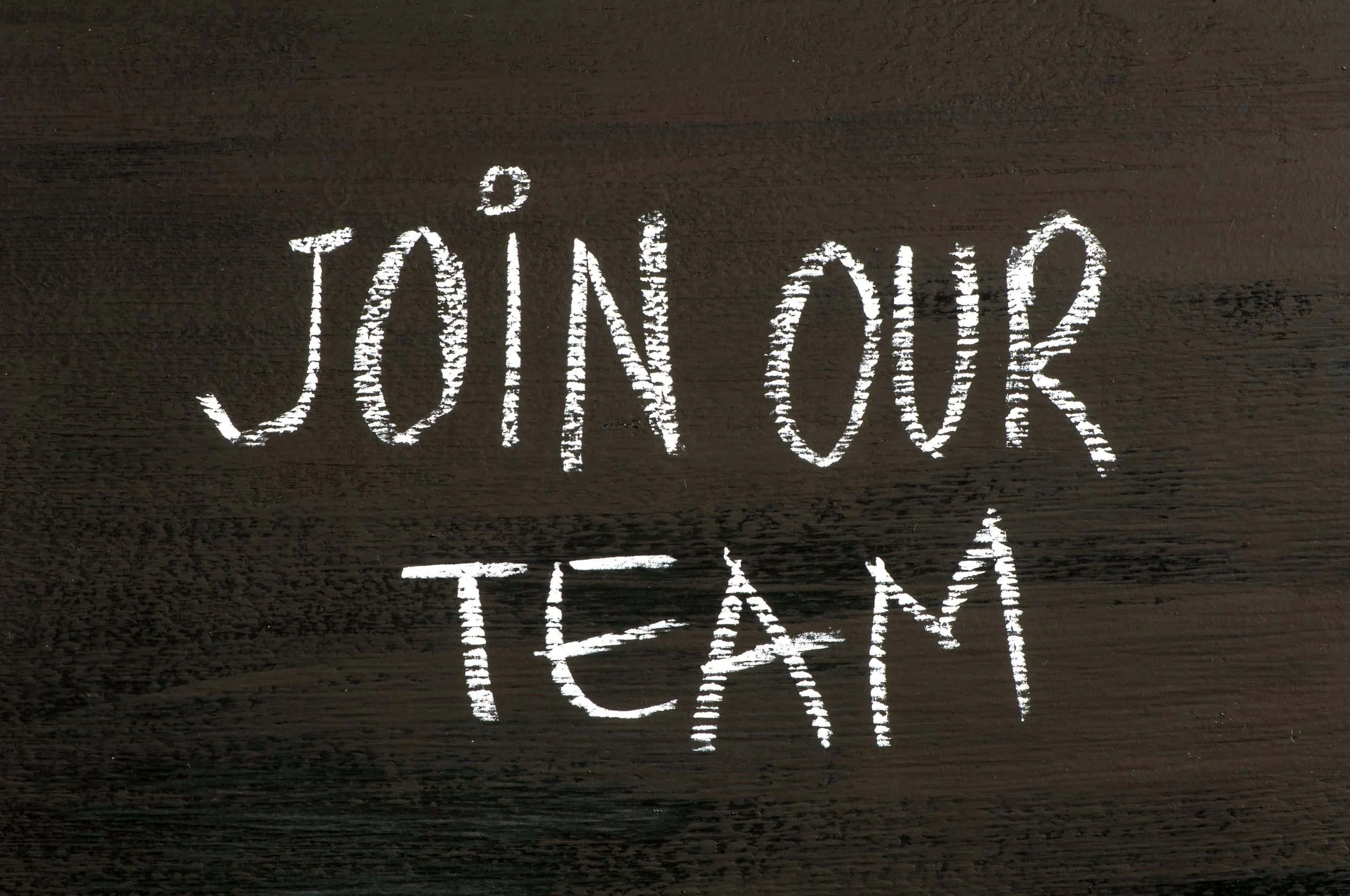 White chalk writing on black surface that says 'Join Our Team'.
