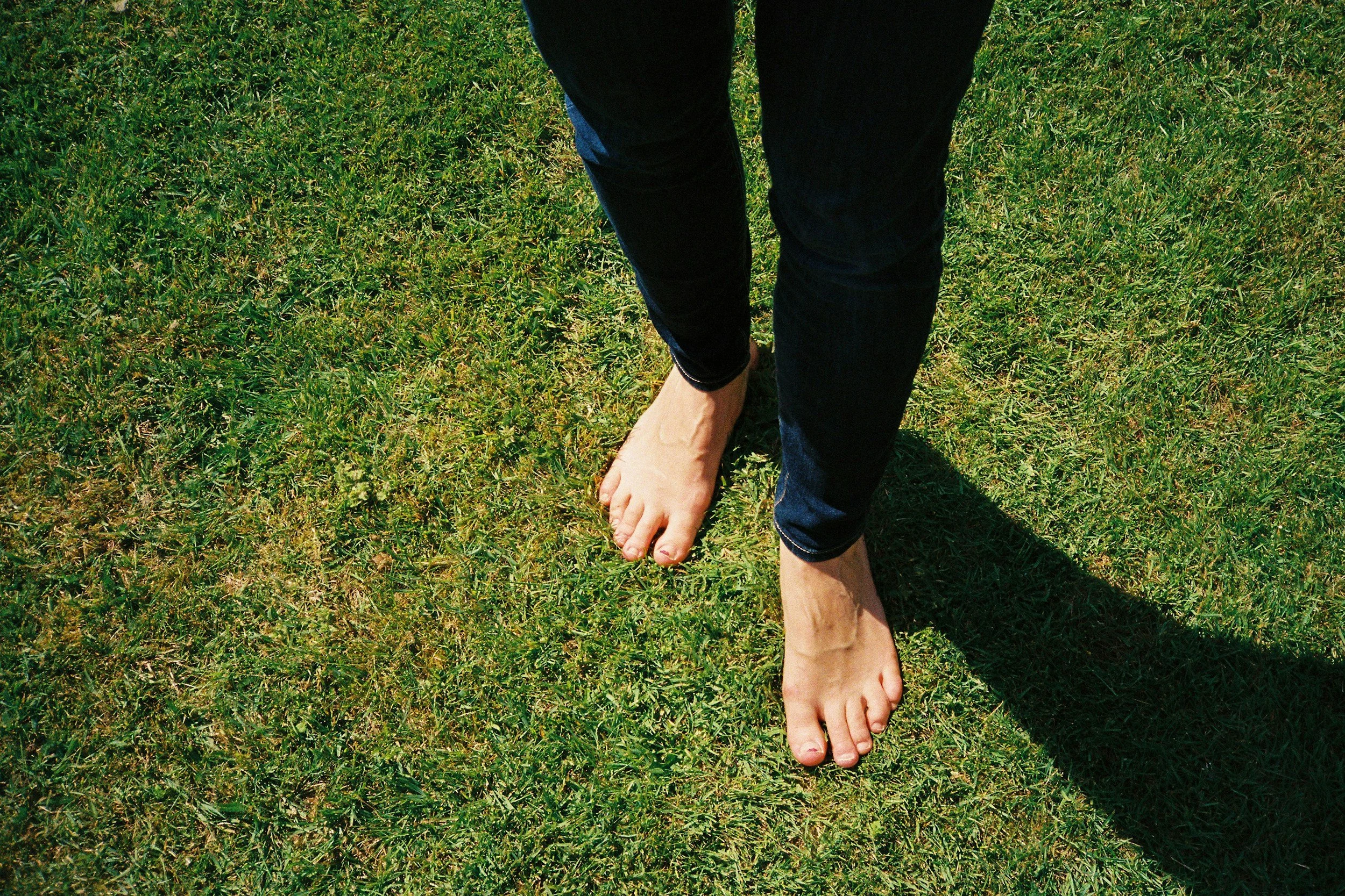 Bare feet walking on green grass outdoors, symbolizing grounding and connection to the present moment.