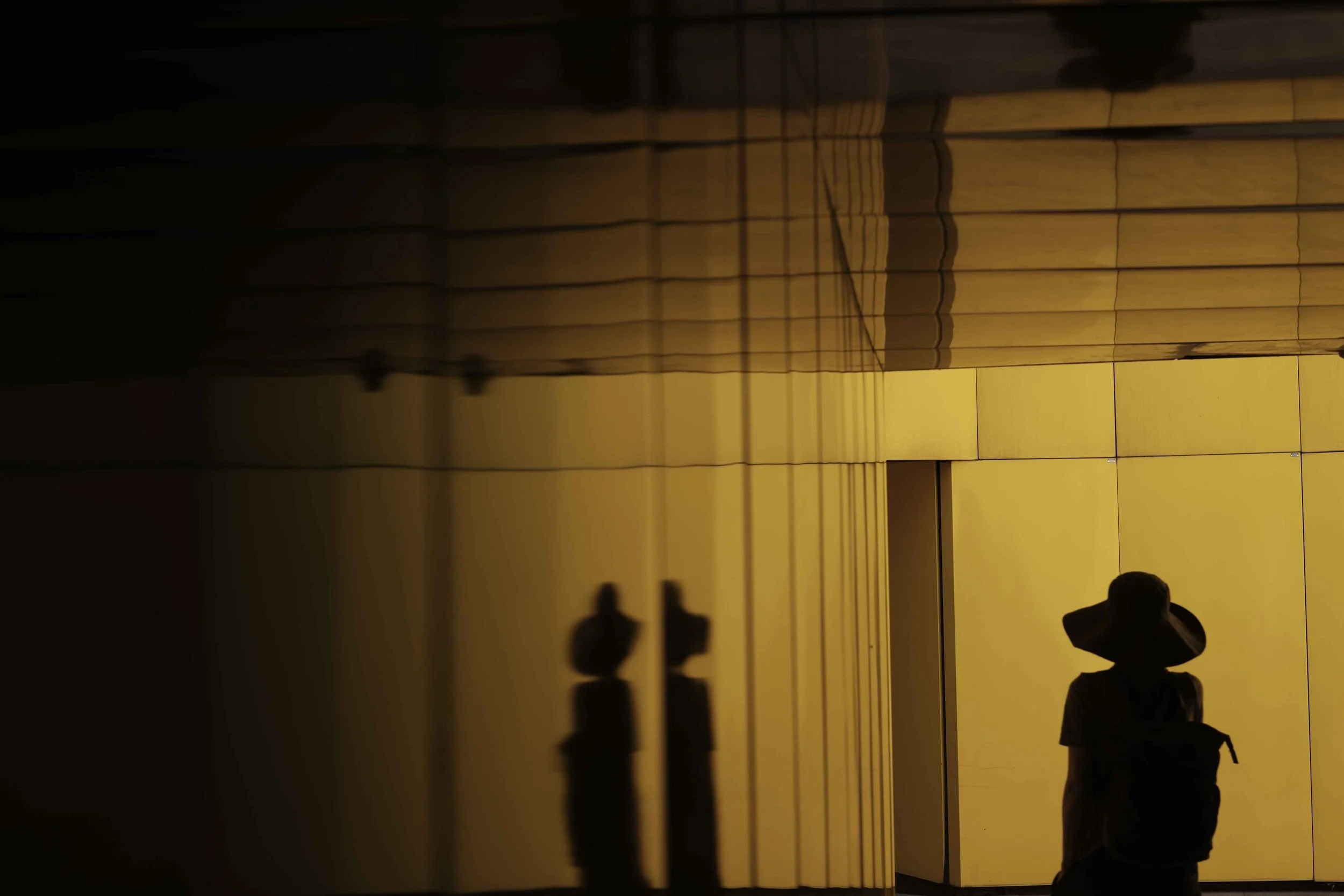 A silhouette of a person wearing a hat walking through a mirrored room.