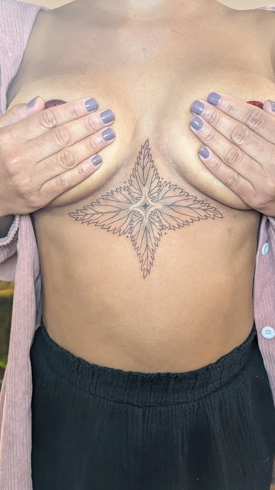 An image of a tattoo on a person center chest. The tattoo is black an grey, of a illustrative nettle, on a mid color skin tone