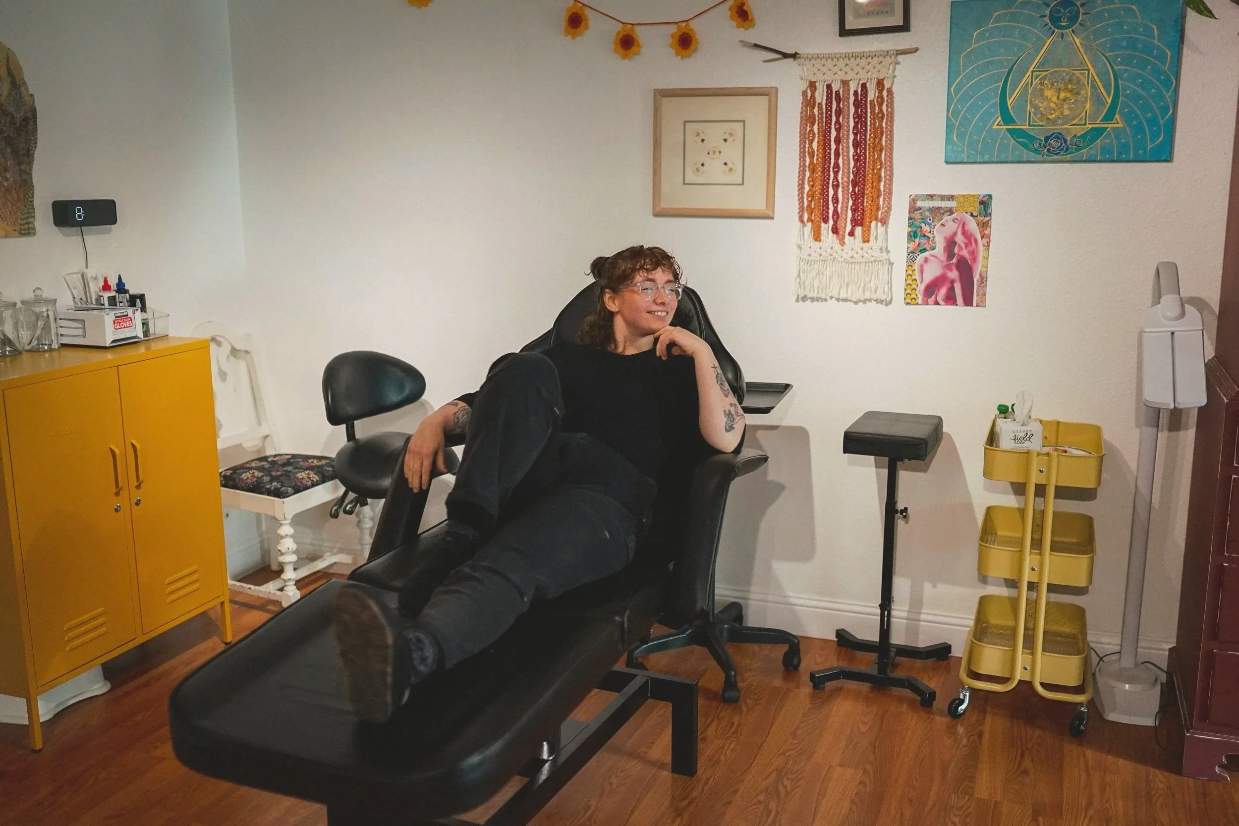 A picture of Rayla, the tattoo artist, lounging in her station with her hand on her chin.