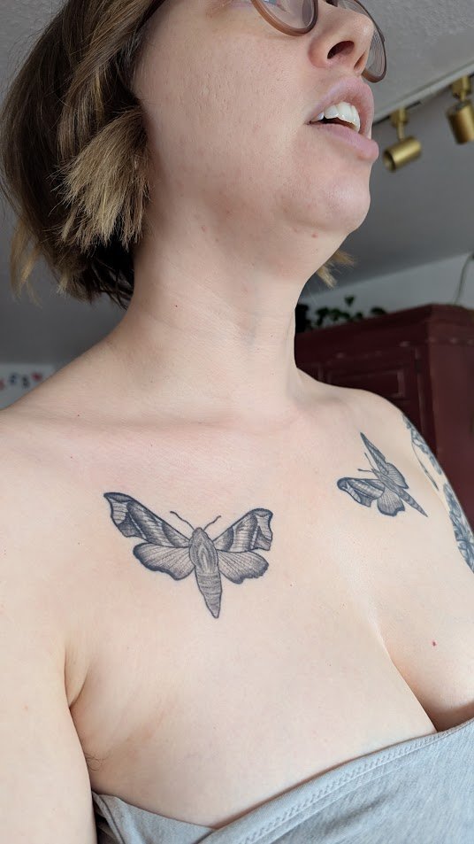 Healed tattoo on a woman's chest, 2 moths in an illustrative style in black and grey ink.
