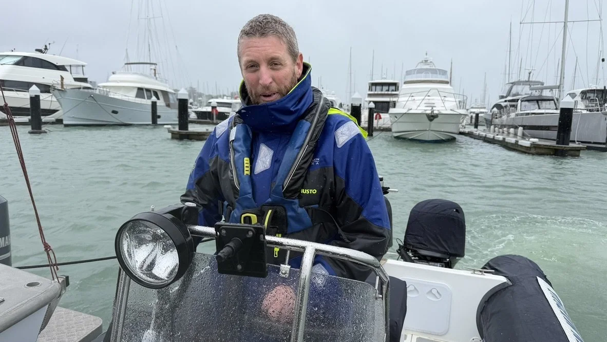 Andrew Flanagan at the helm of a RIB wearing a lifejacket, Westhaven Marina, Auckland