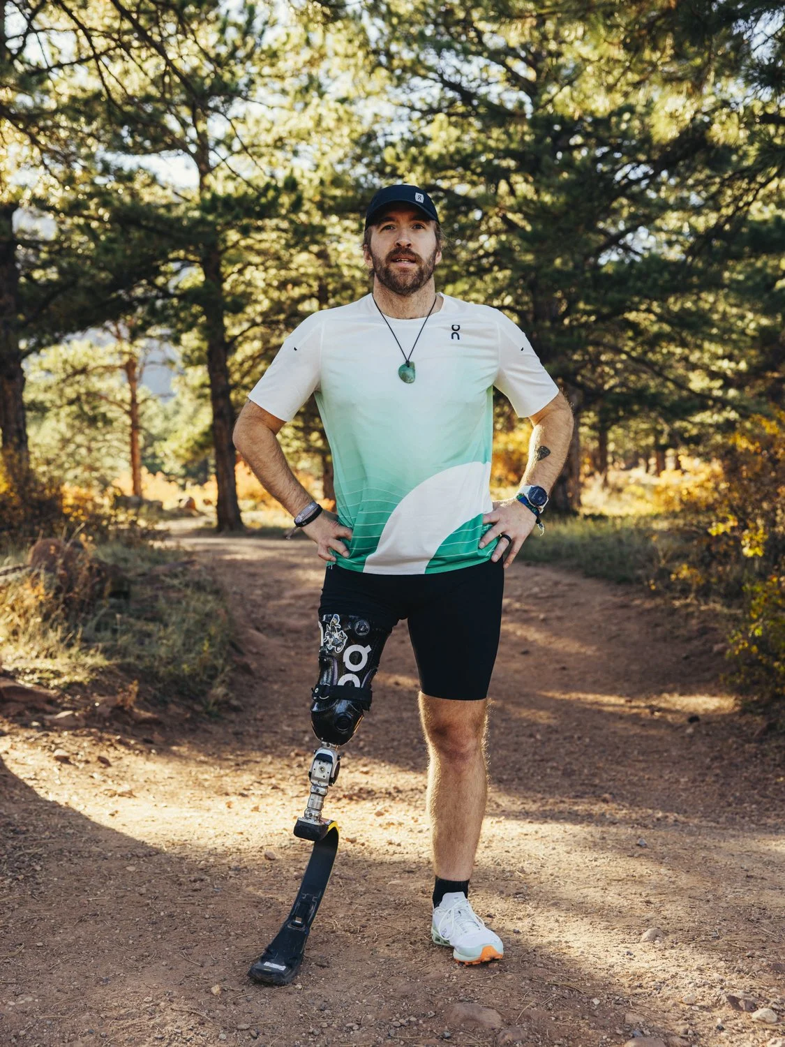 Zach standing on trail with green t-shirt and ON tights with blade and blurry trees in background