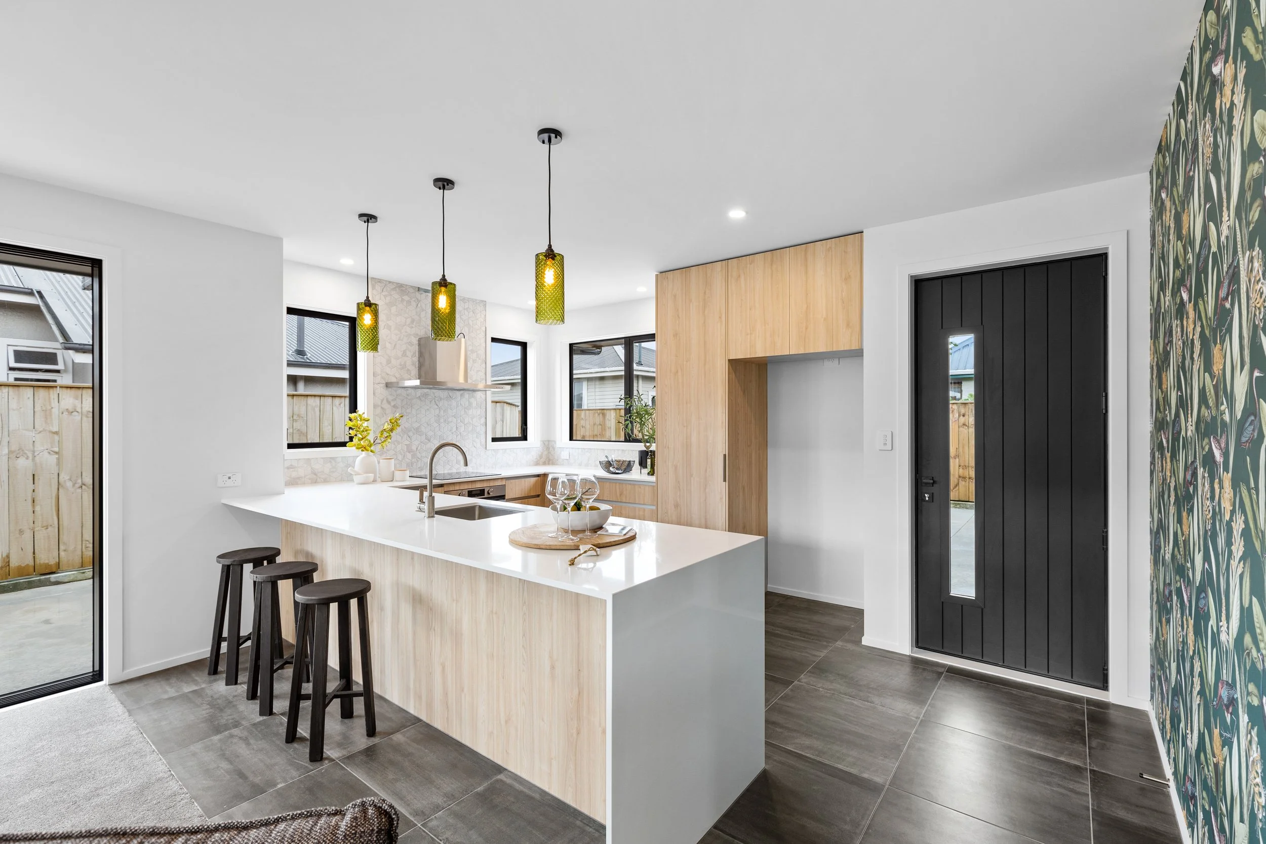 Modern kitchen with white island and natural wood accents, black front door, and floral accent wall.