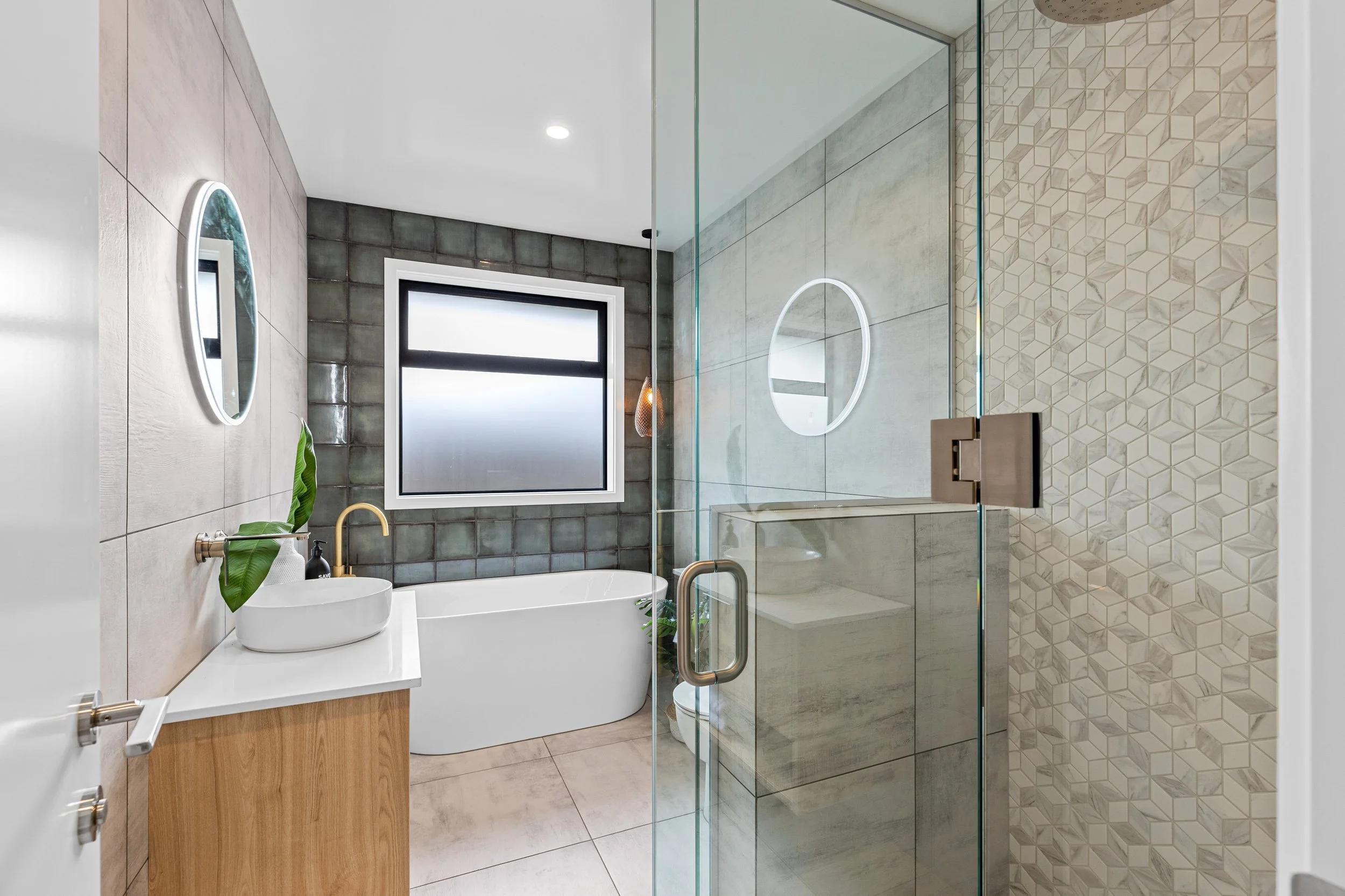 Modern bathroom with a freestanding bathtub, a vanity with a vessel sink, and a glass shower enclosure with geometric tile walls.