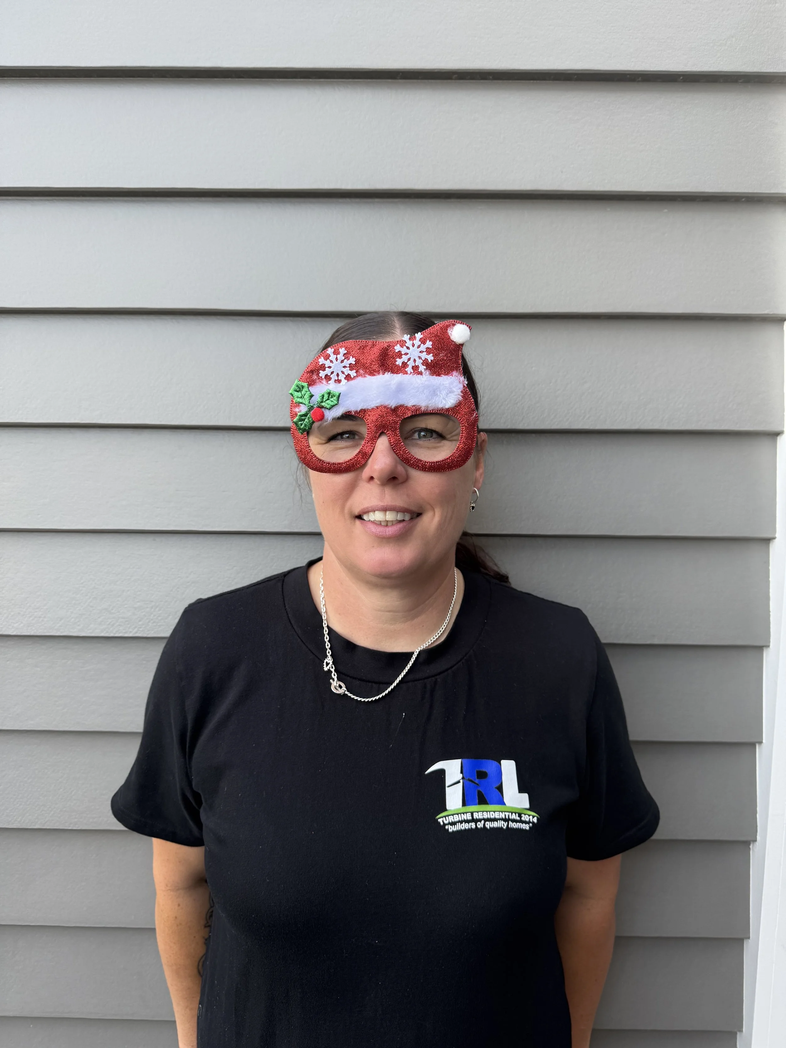 Woman wearing novelty red glasses with Christmas decorations, standing in front of gray horizontal siding.