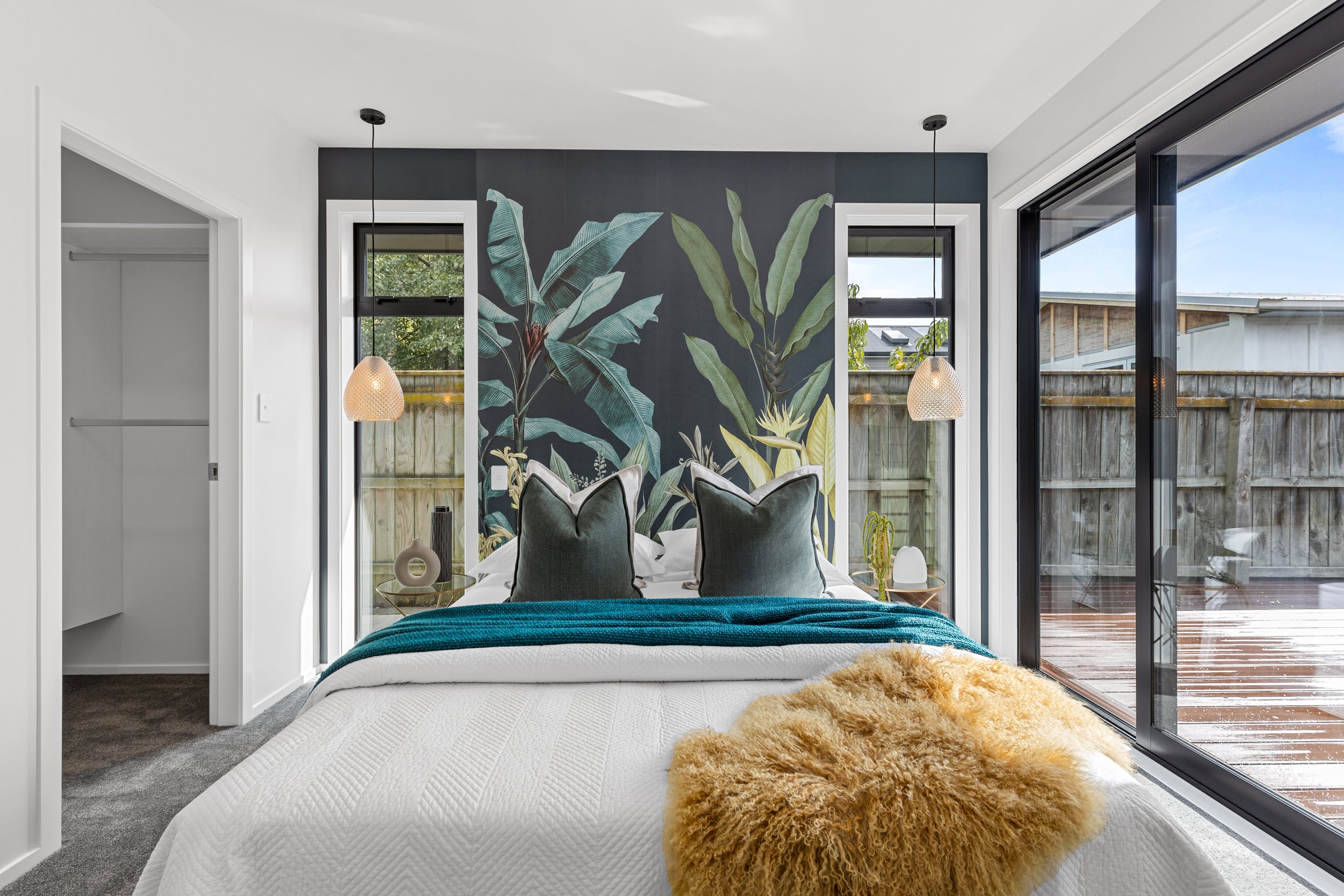 Modern bedroom with botanical mural behind bed, large glass sliding door to outdoor deck, and minimalist decor.