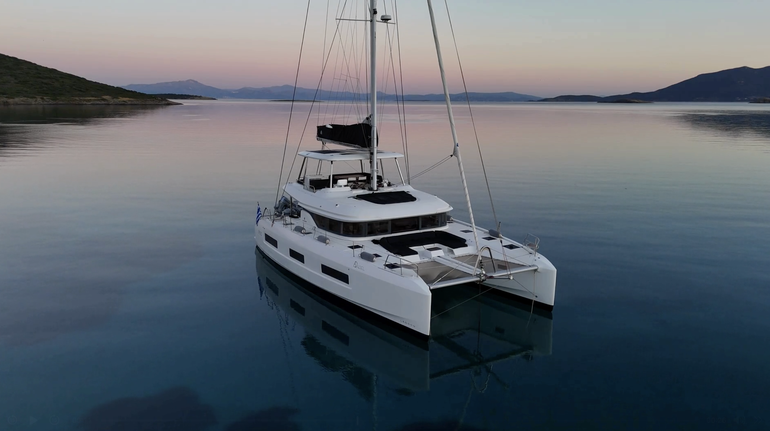 A luxurious white sailing yacht floating on calm water during sunset, with a mountainous landscape and a soft pastel sky in the background.