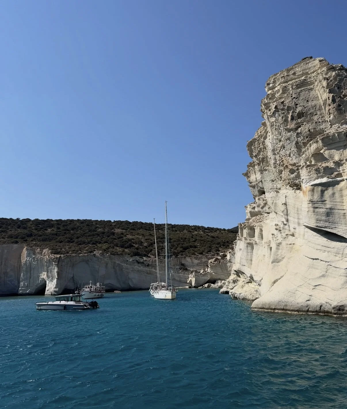 Sailboats anchored near white cliffs along a clear blue sea with a bright sky.