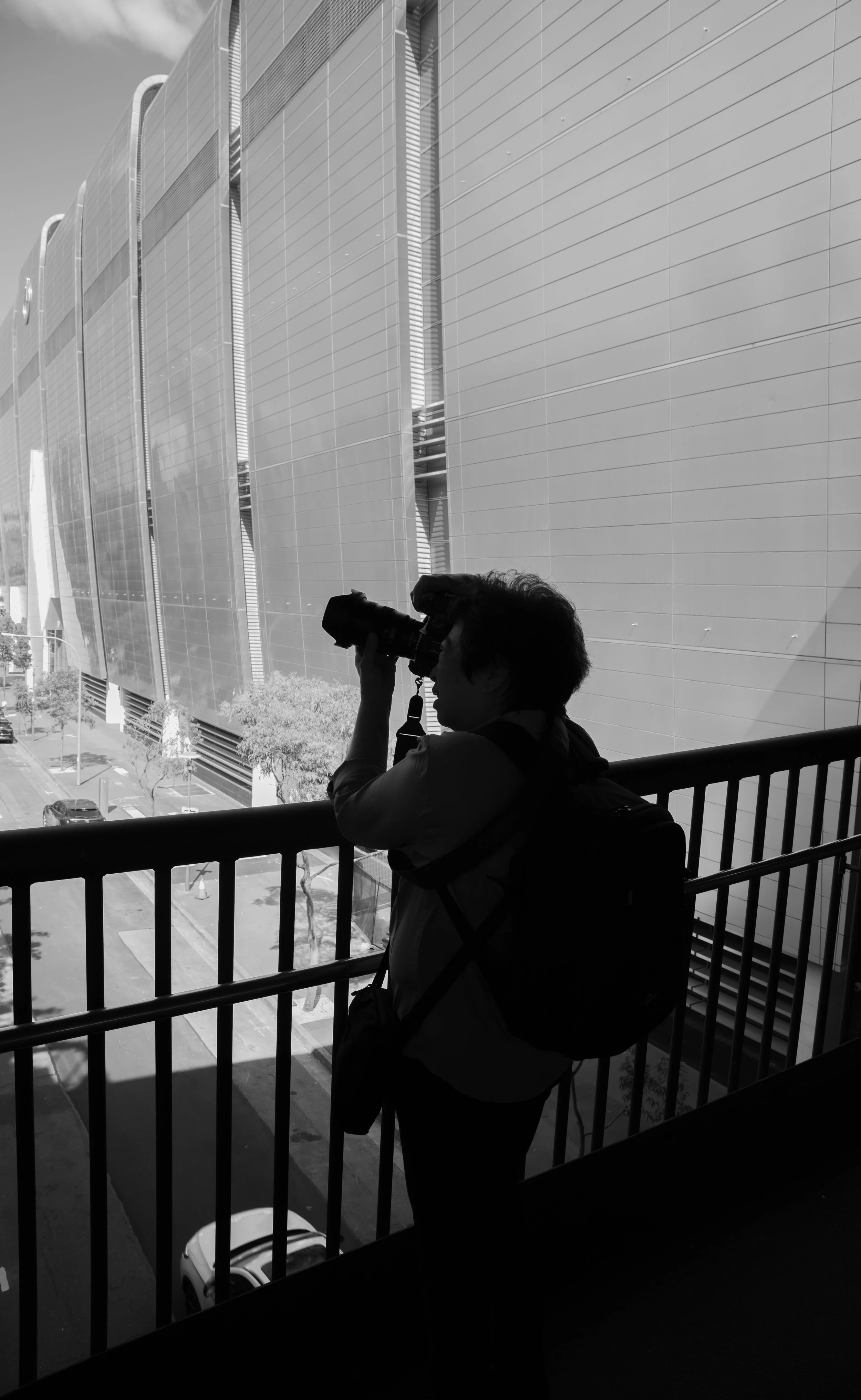Silhouette of a person taking a photograph on a balcony overlooking a modern building with large panels.