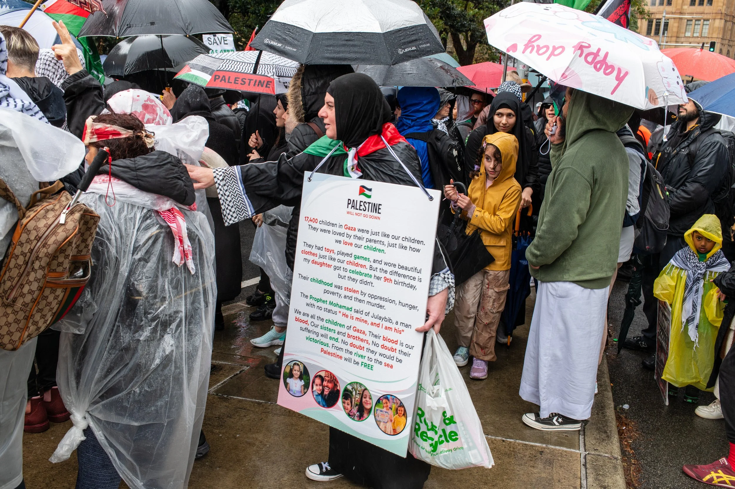 A crowd of people protesting with umbrellas on a rainy day, holding signs and wearing rain gear.