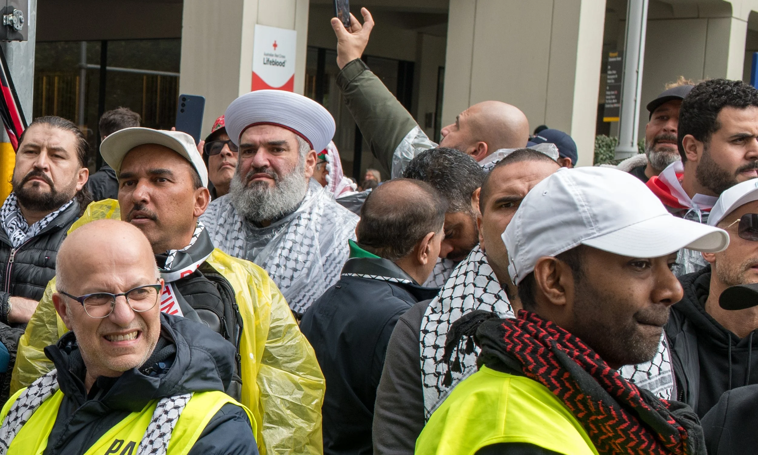 Group of people participating in a protest or rally, wearing high visibility vests and scarves with various expressions.