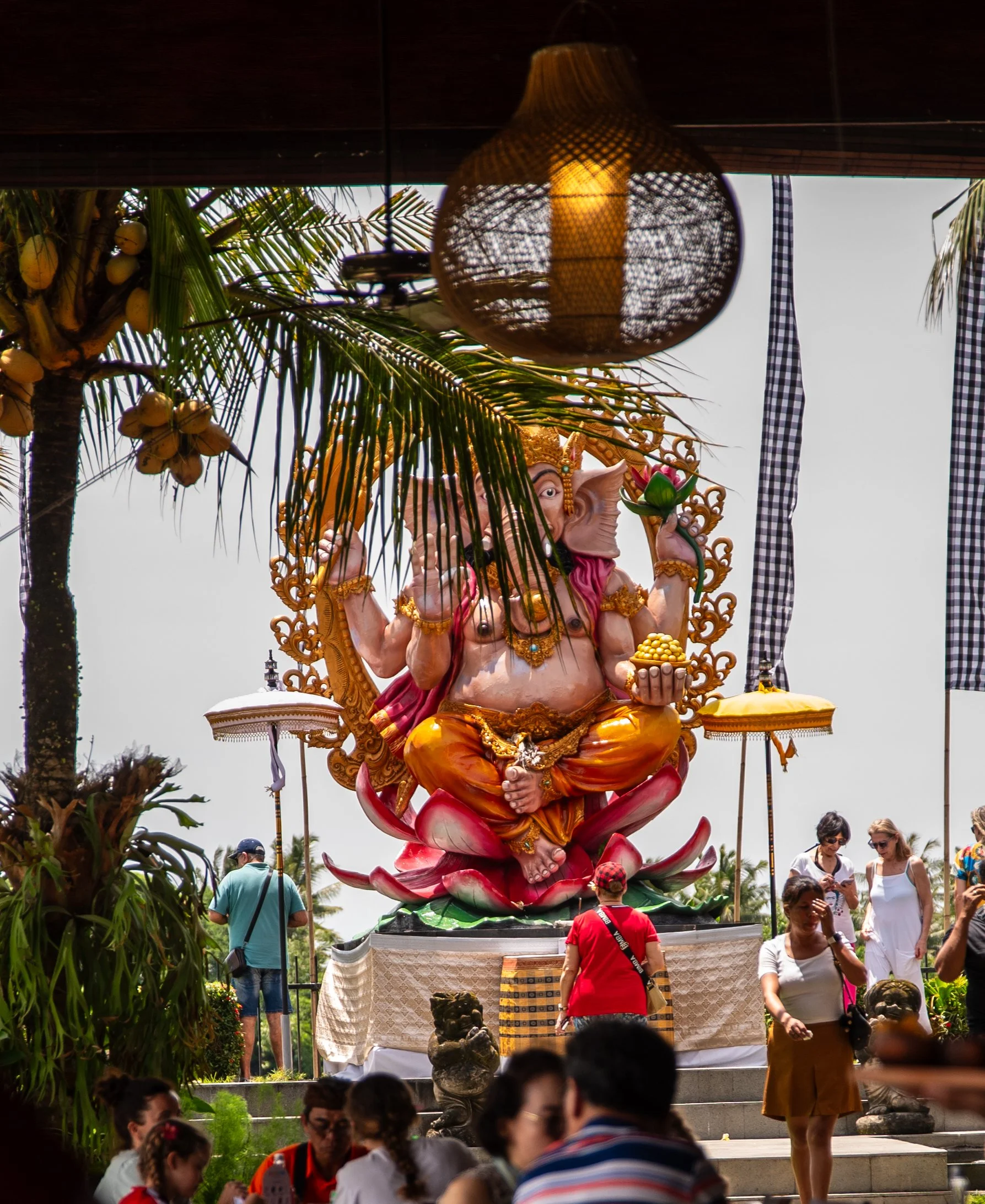 Large colorful statue of Ganesha, the Hindu god with an elephant head, seated on a pedestal with people surrounding it during a daytime outdoor festival or celebration.