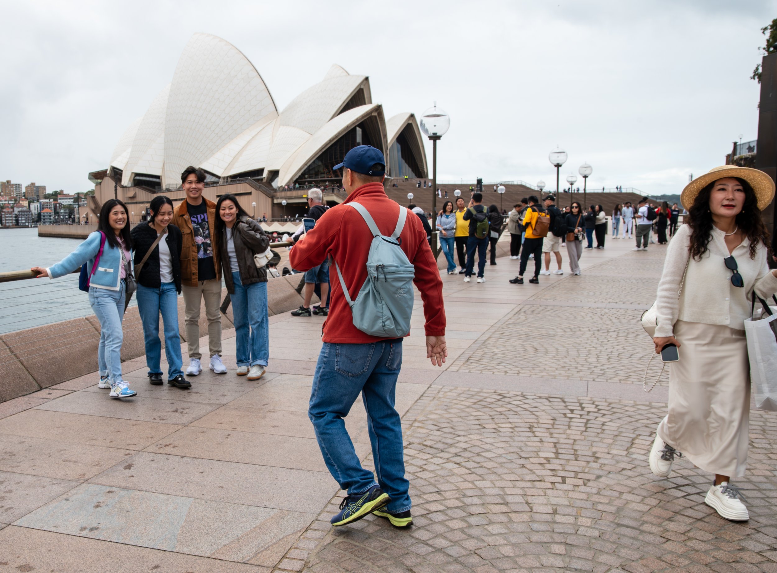 Tourists taking photos near Sydney Opera House with overcast sky