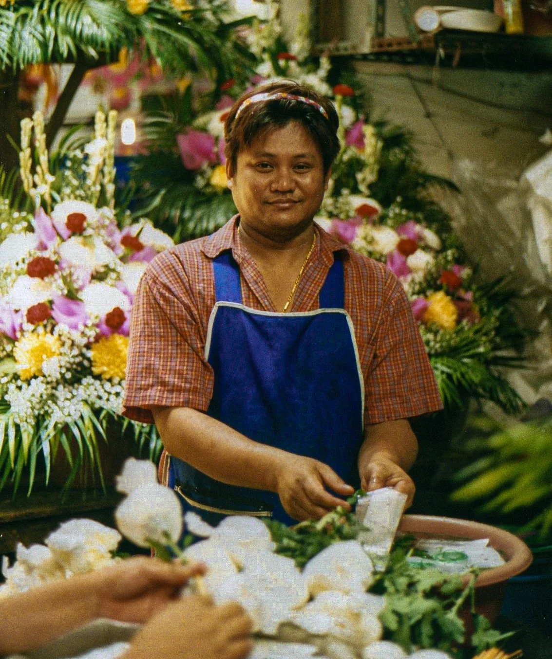 A person working at a flower stall with colorful floral arrangements in the background.