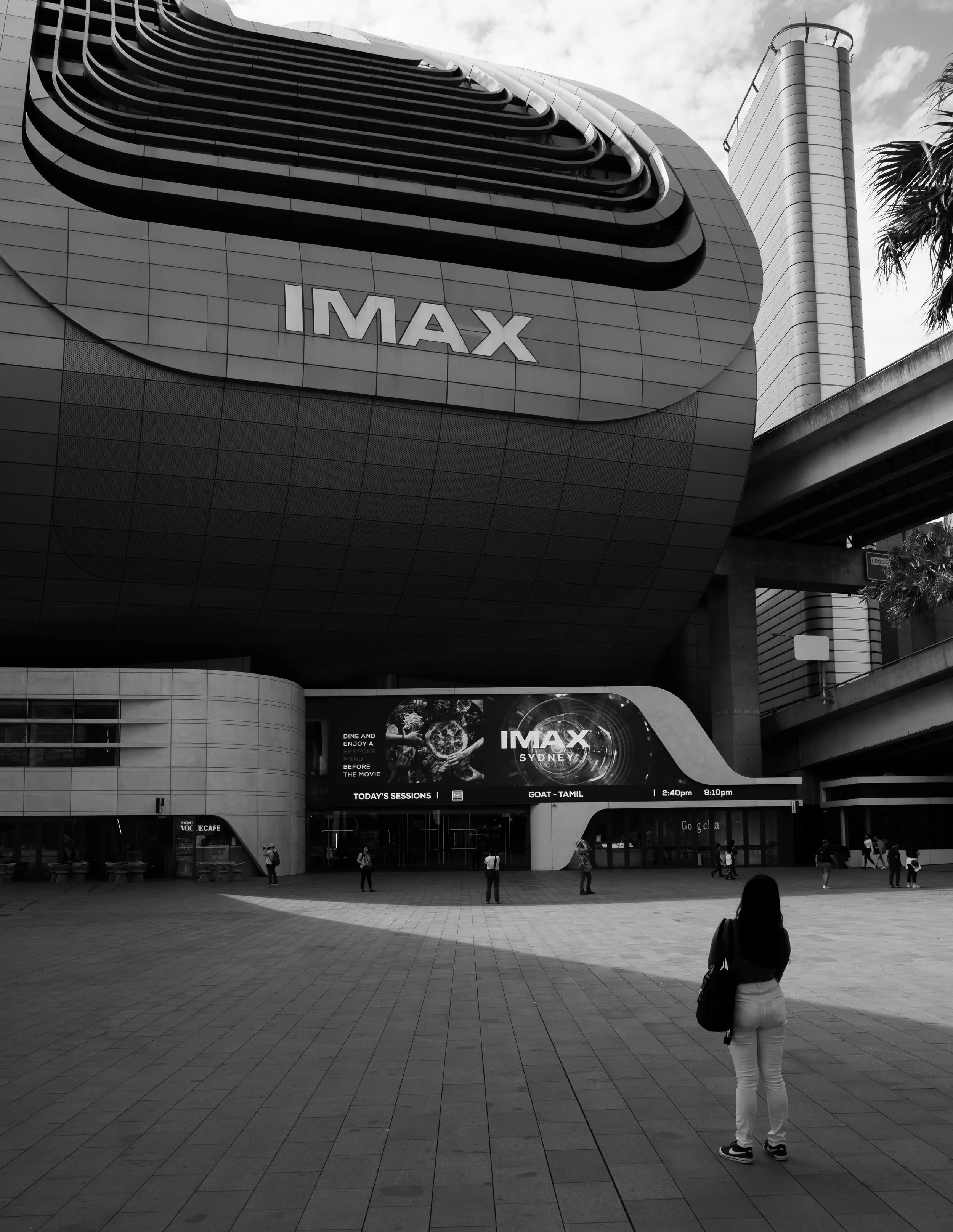 Exterior view of an IMAX cinema building in Sydney, with people walking in front of it, in black and white.