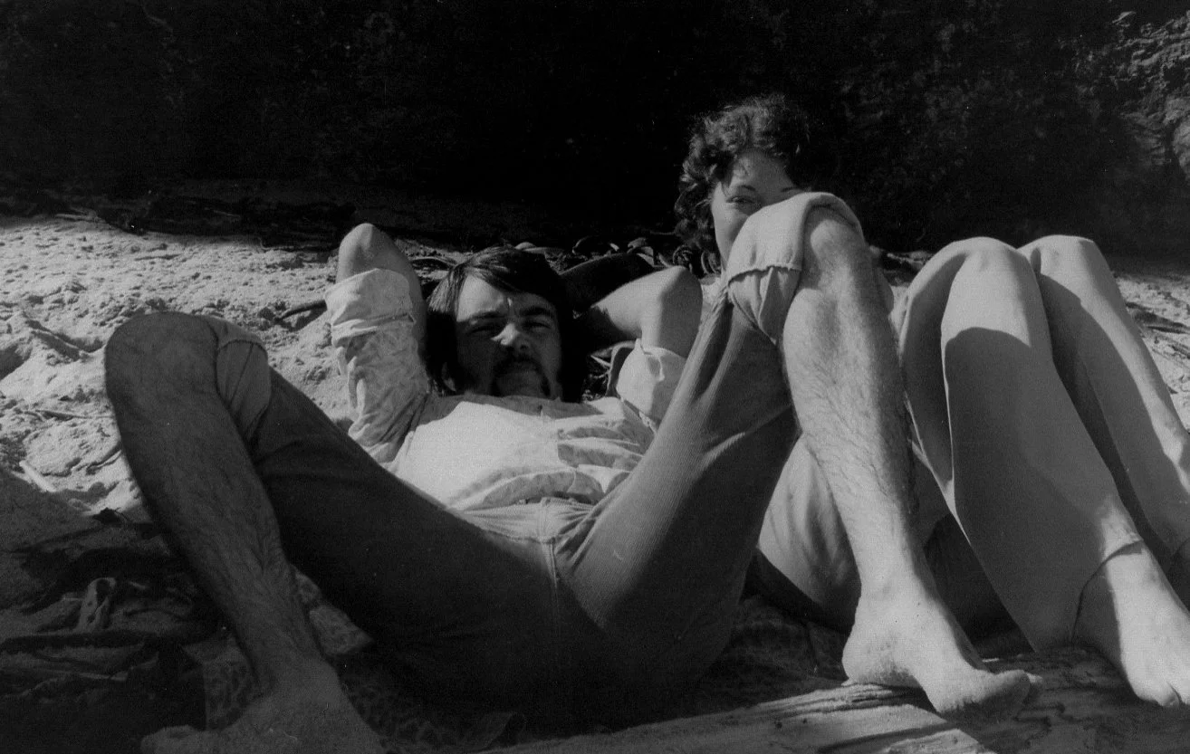 Black and white photo of a man and woman lying on a sandy beach, possibly from the mid-20th century, with rocks in the background.